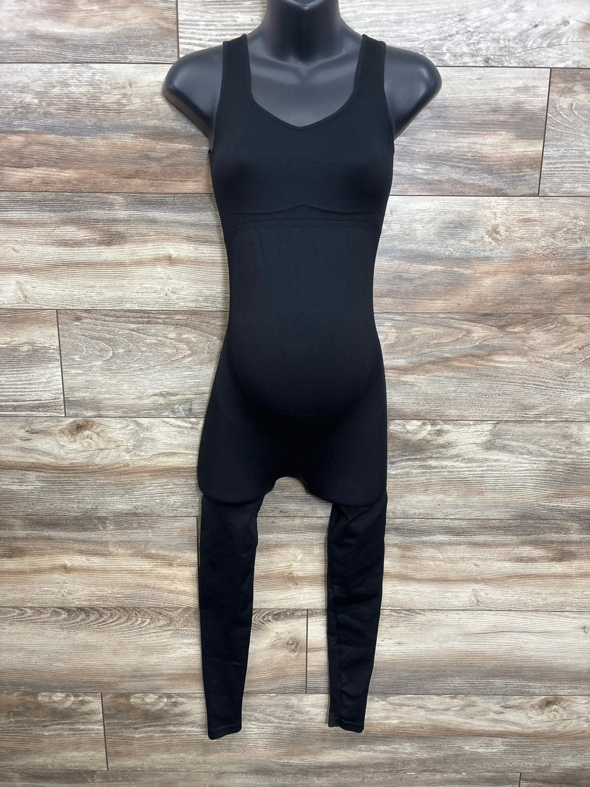 Front view of black maternity unitard with compression fabric and fitted belly panel on mannequin against wood background