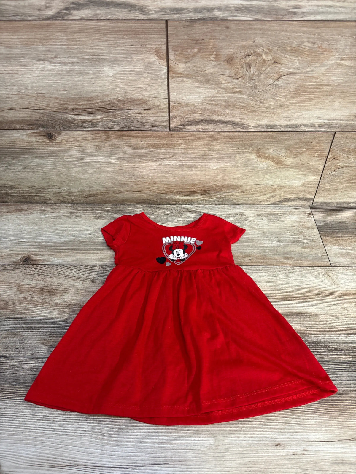 Front view of red Disney Baby Minnie dress size 18 months with Minnie Mouse graphic and gathered skirt on wood floor