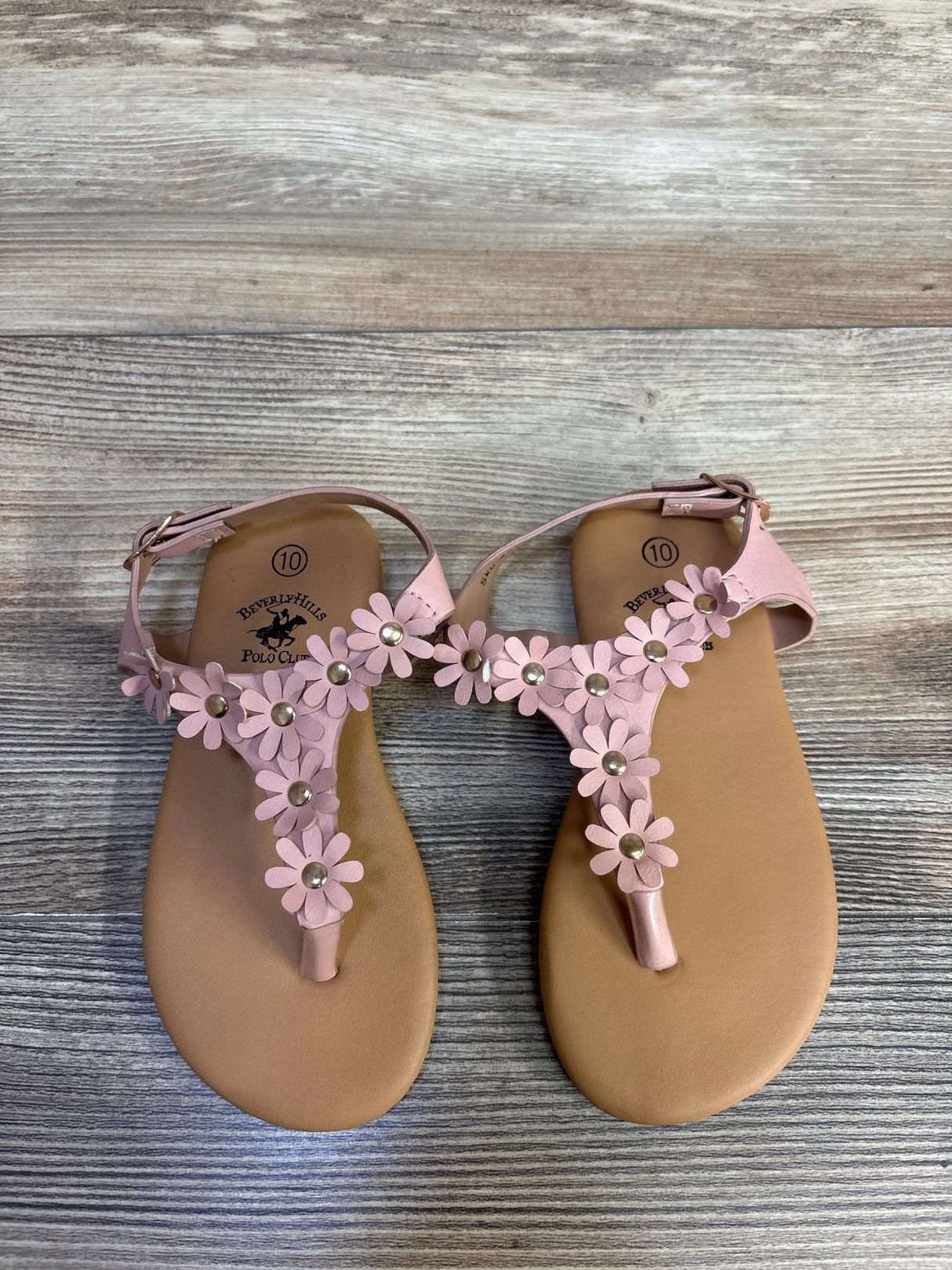Overhead view of Beverly Hills Polo Club pink toddler sandals showcasing daisy floral straps with gold studs on wood-grain background, size 10C