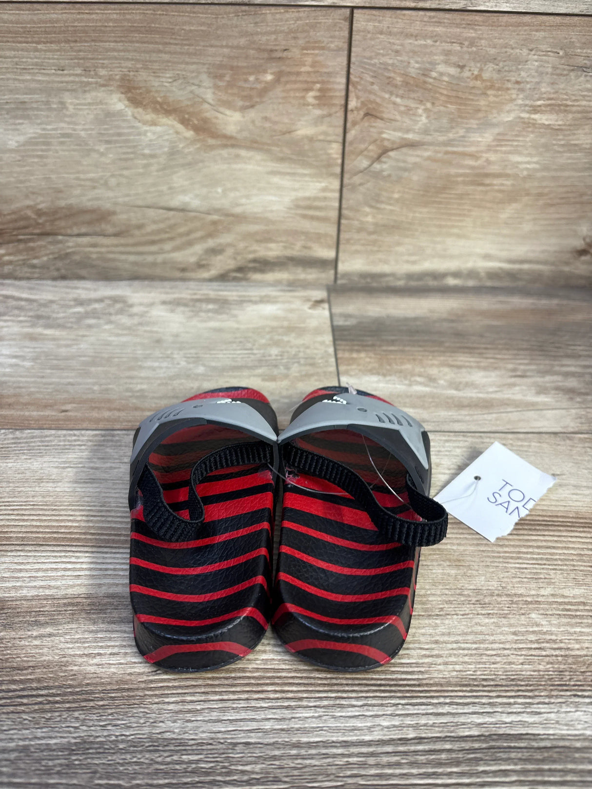 Front view of toddler Shark slide sandals with red and black striped footbed, gray upper and black heel straps on wood floor
