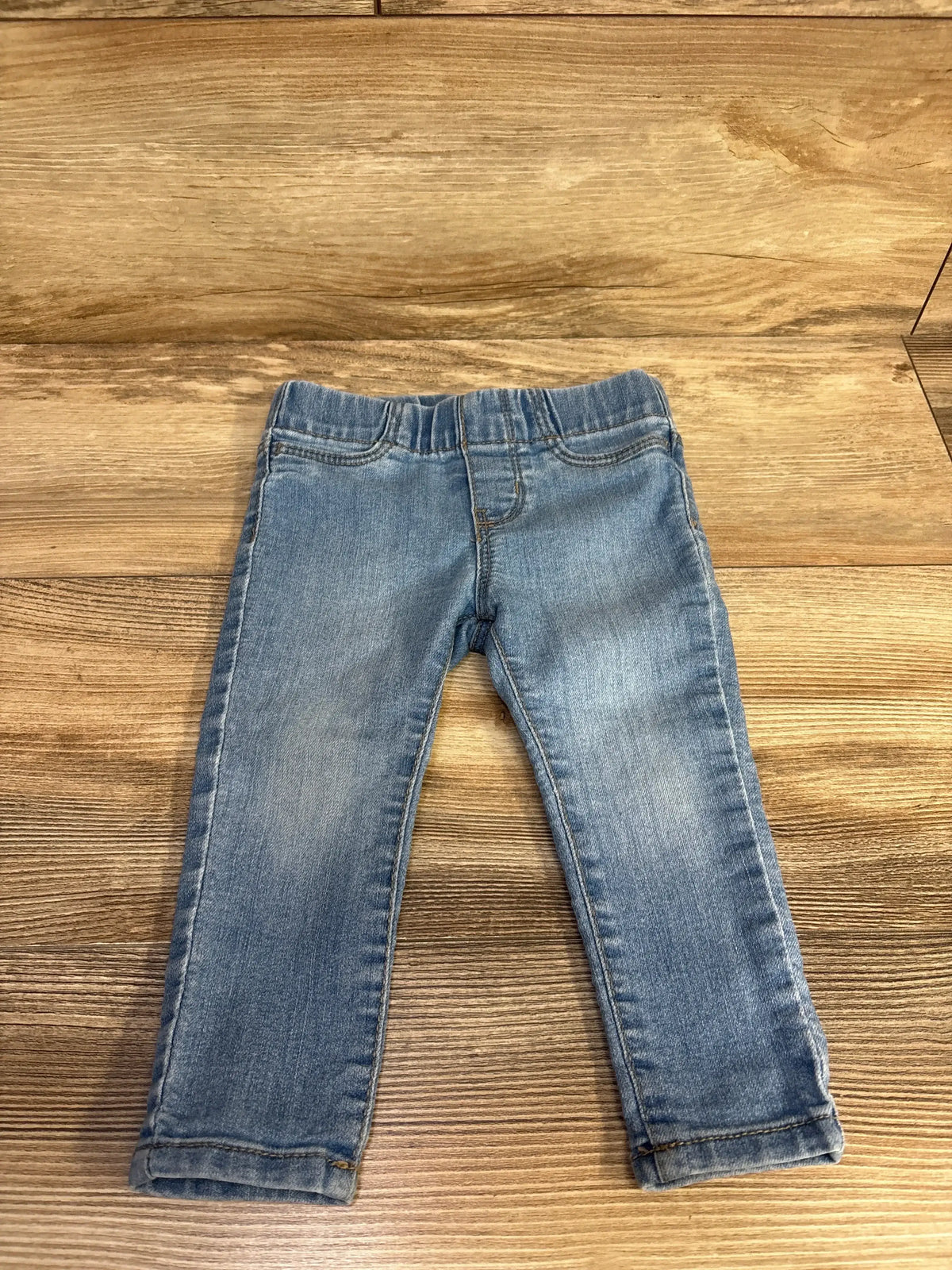Front view of Oshkosh blue toddler jeggings showing elastic waistband and slim legs on wood background