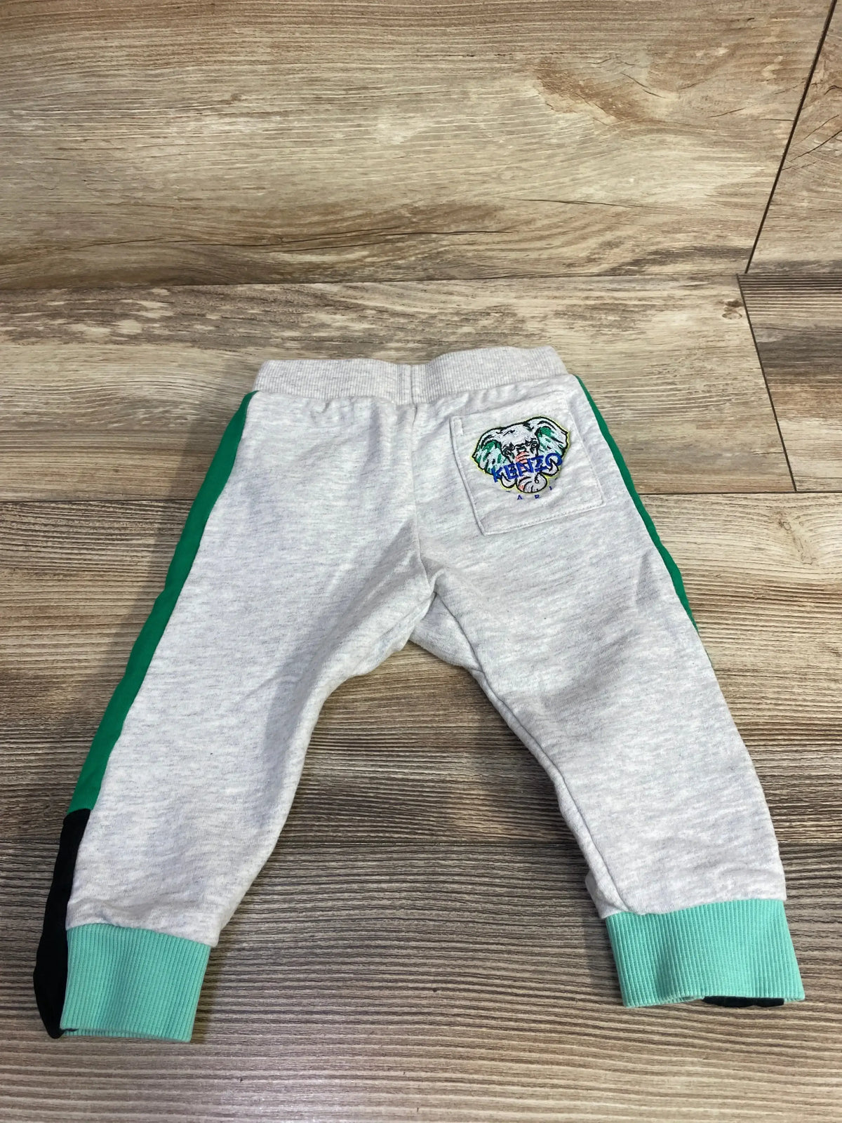 Light gray baby joggers with teal cuffs, green side stripes, and a sports logo patch on back pocket