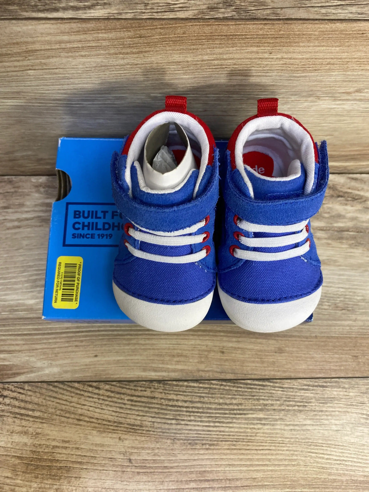Top view of NEW Stride Rite Soft Motion Danny sneakers in blue with red accents on original box atop wood plank floor