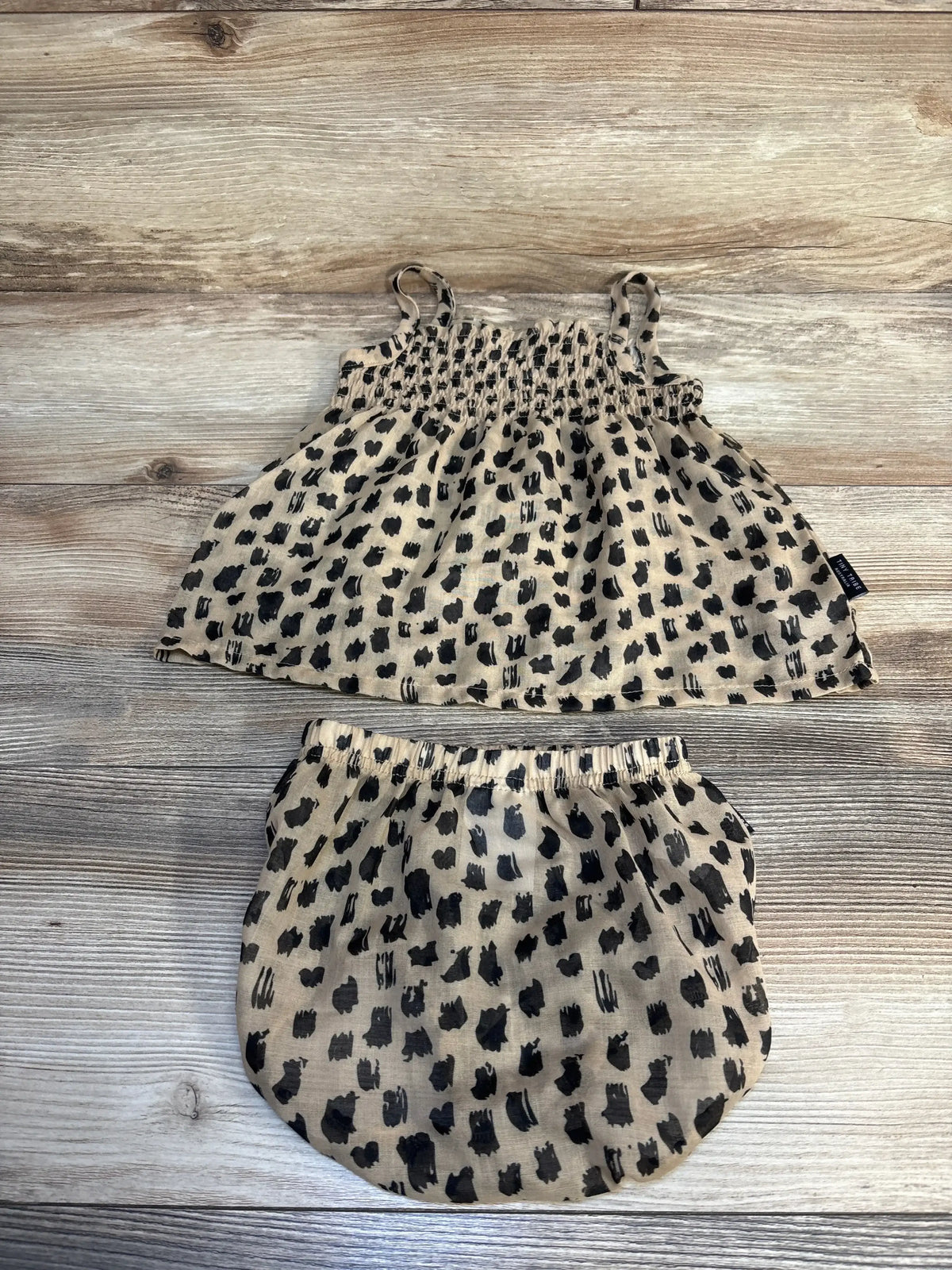 Top-down view of Tiny Tribe Australia cheetah print dress and bloomers 2pc set in tan showcasing black spotted print on a wood background