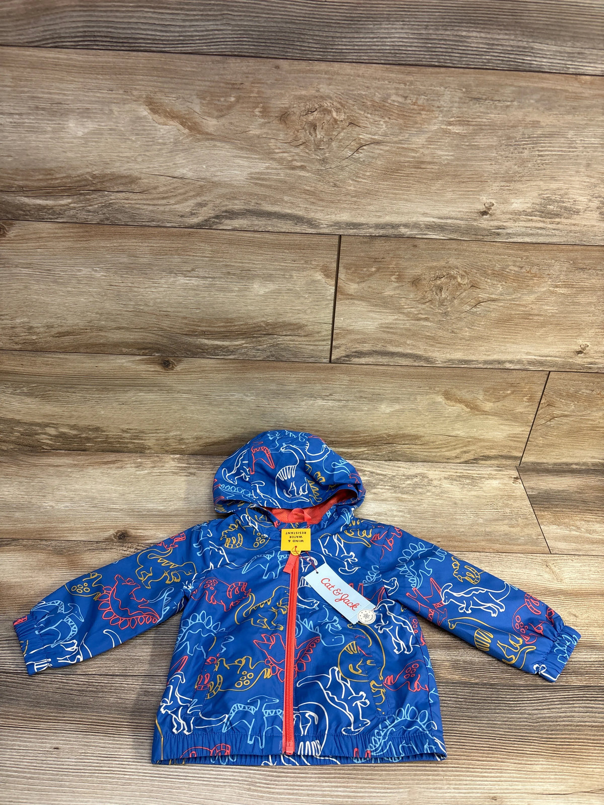 Front view of Cat & Jack blue toddler dinosaur windbreaker jacket with hood and red zipper laid flat on wooden floor
