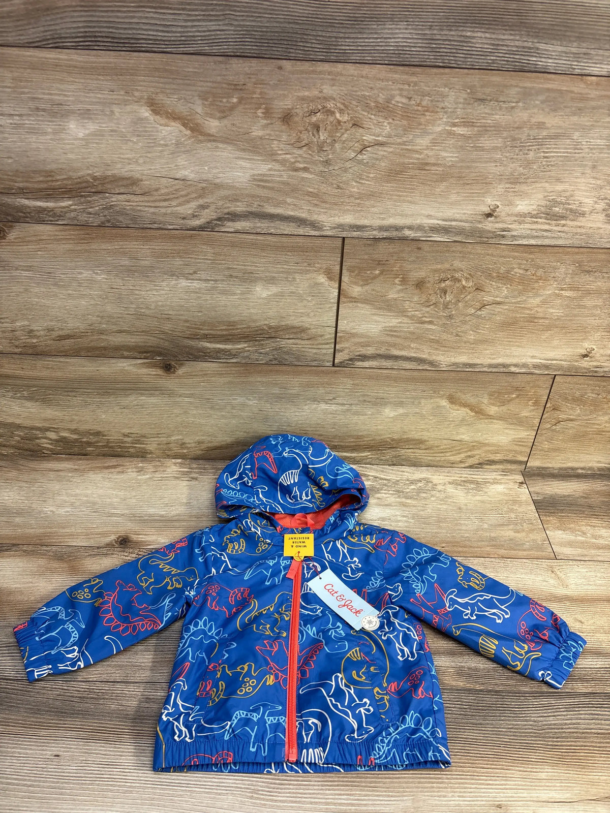 Front view of Cat & Jack blue toddler dinosaur windbreaker jacket with hood and red zipper laid flat on wooden floor