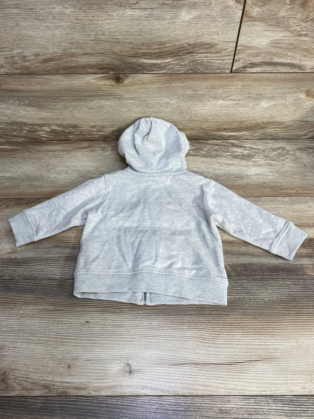 Back view of Tommy Hilfiger baby full-zip hoodie in light grey showing hood, ribbed cuffs and hem on wood plank background
