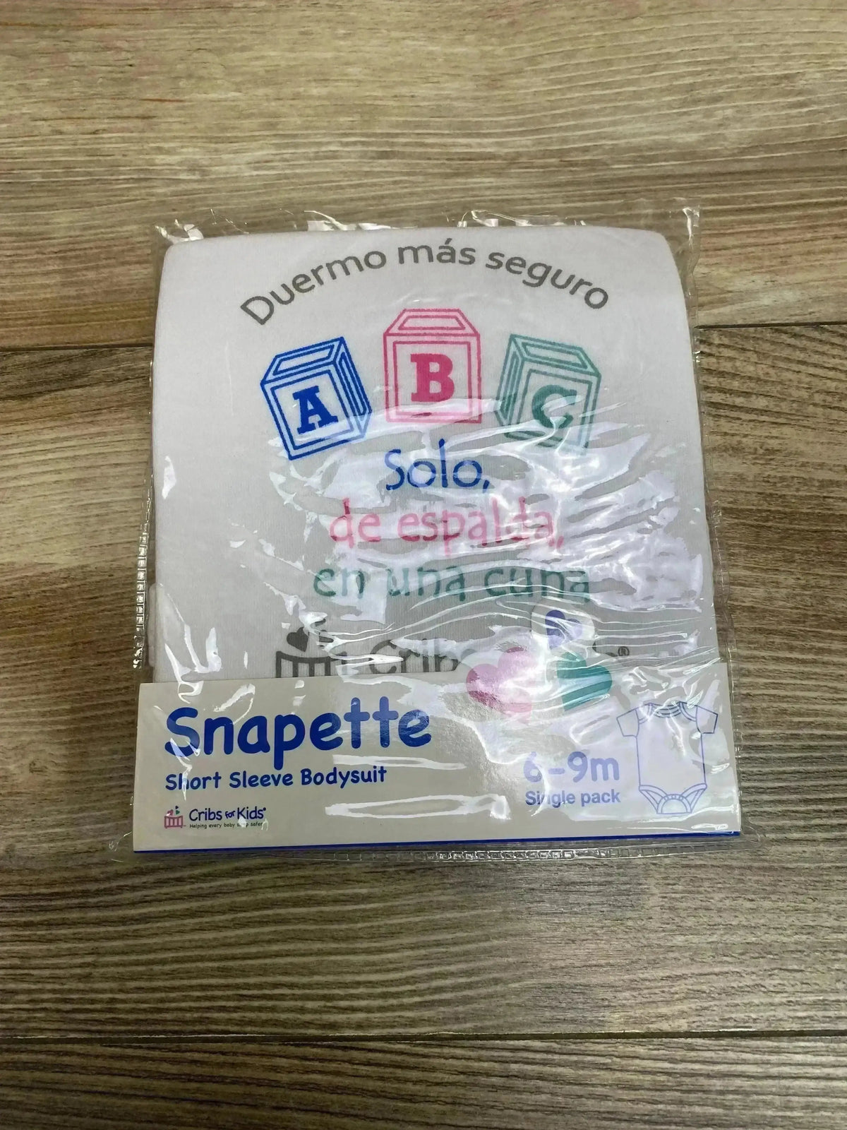 Top view of Snapette white short-sleeve bodysuit with printed ABC blocks, folded in original plastic packaging on wood floor