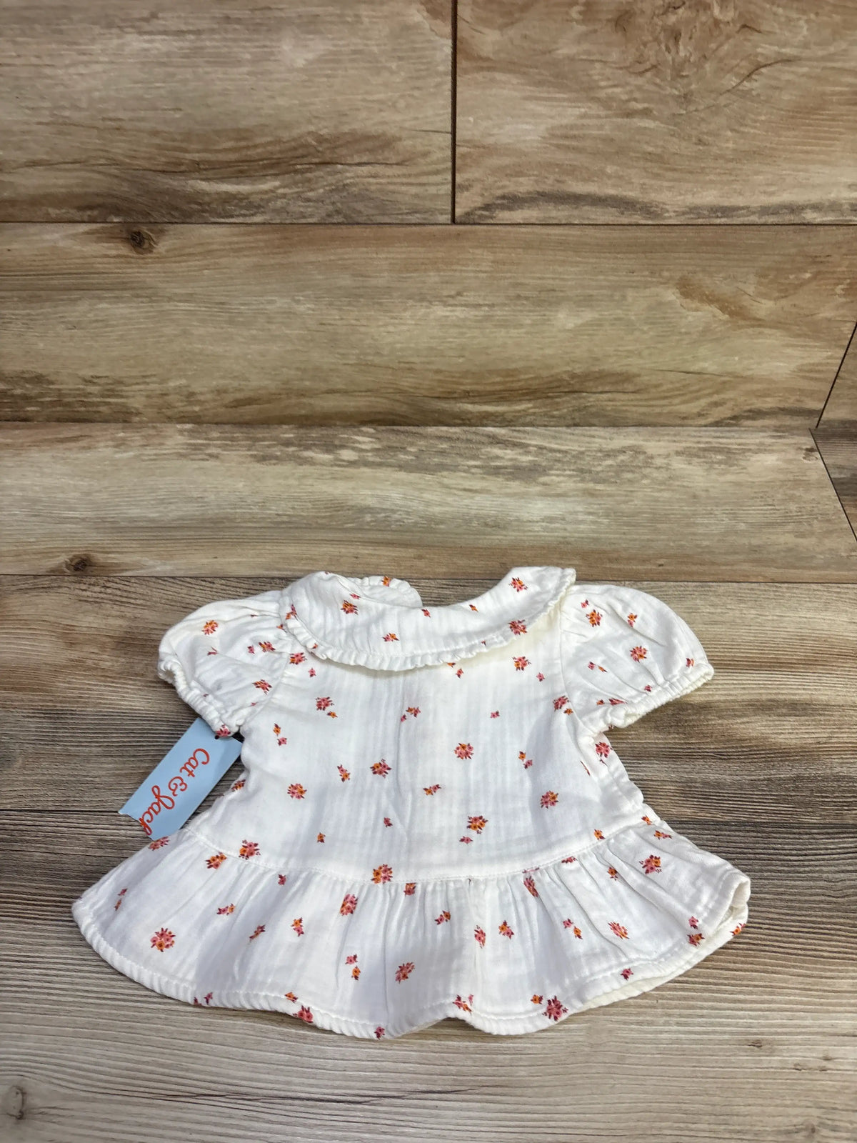 Front view of Cat & Jack white gauze button-front peplum top with floral print and puff sleeves on wood background