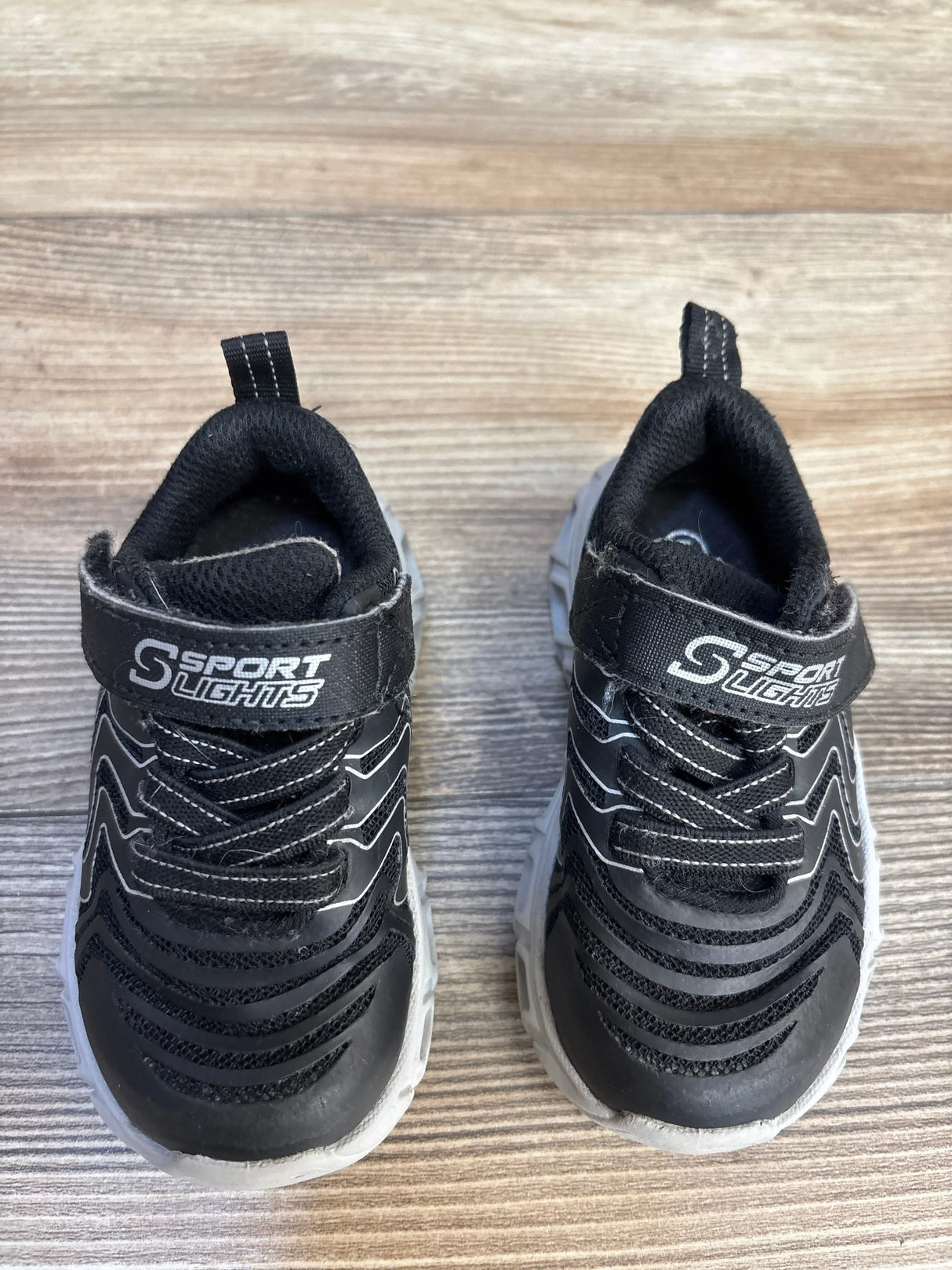 Pair of black kids' Sport Lights athletic shoes with white soles on wood surface