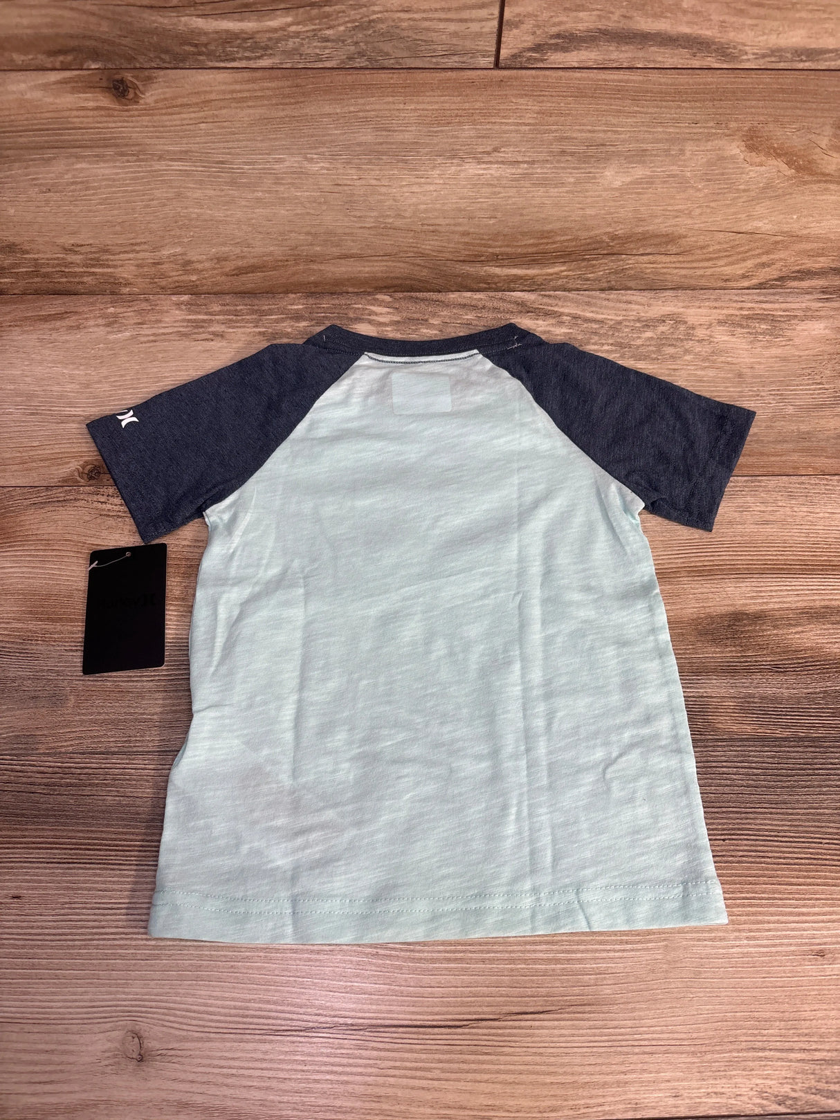 Back view of kids' short sleeve raglan t-shirt with light blue body and dark blue sleeves on wooden floor