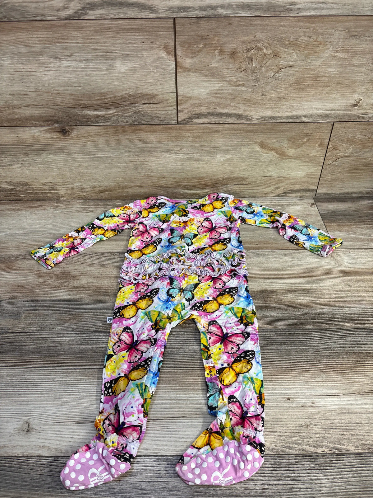 Top view of Bums & Roses butterfly ruffle footie, size 18-24 months, with ruffles and footed legs on a wooden floor