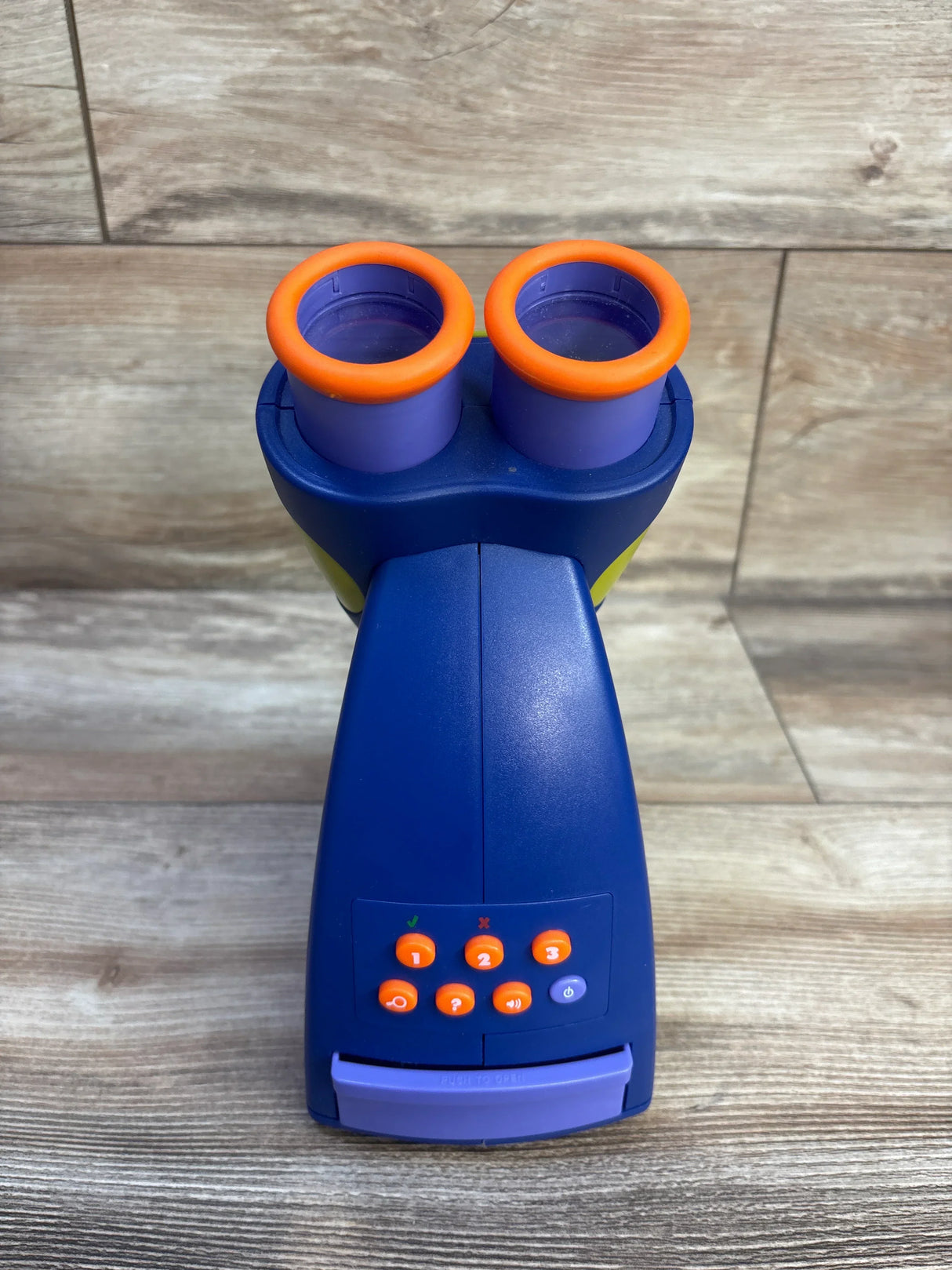 Front view of GeoSafari Jr. talking microscope with dual eyepieces with orange rims and control buttons on wood floor