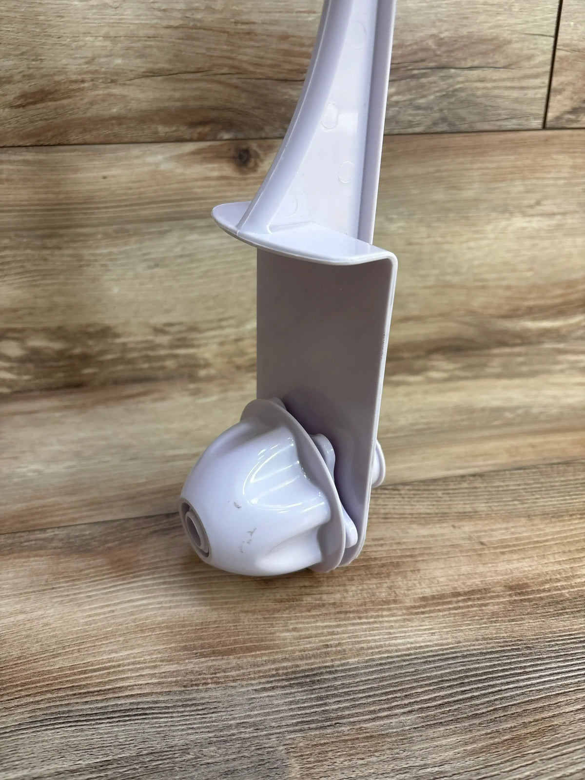 Close-up of crib mobile arm and swivel joint showcasing the white plastic clamp and rotating attachment on wood background