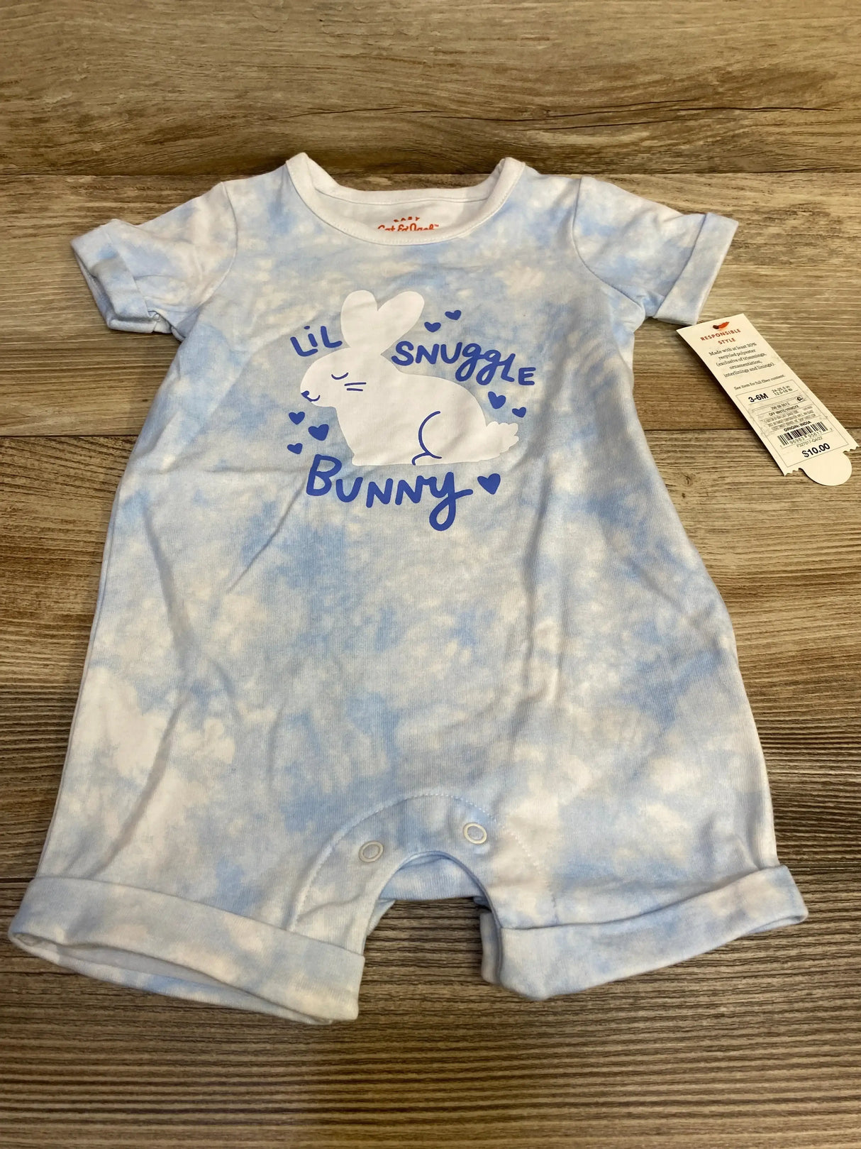 Front flat lay of Cat & Jack baby romper in light blue tie-dye with Lil Snuggle Bunny graphic and crotch snaps on wood background