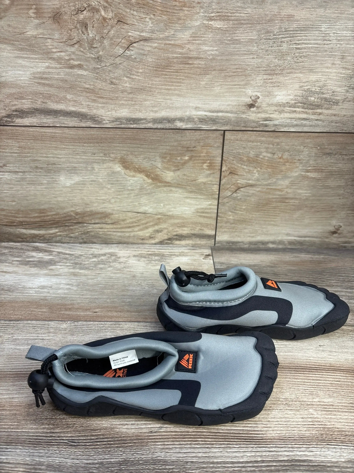 Angled top view of RBX grey water shoes size 11-12C showing toggle closure, black accents and rubber sole on wood floor