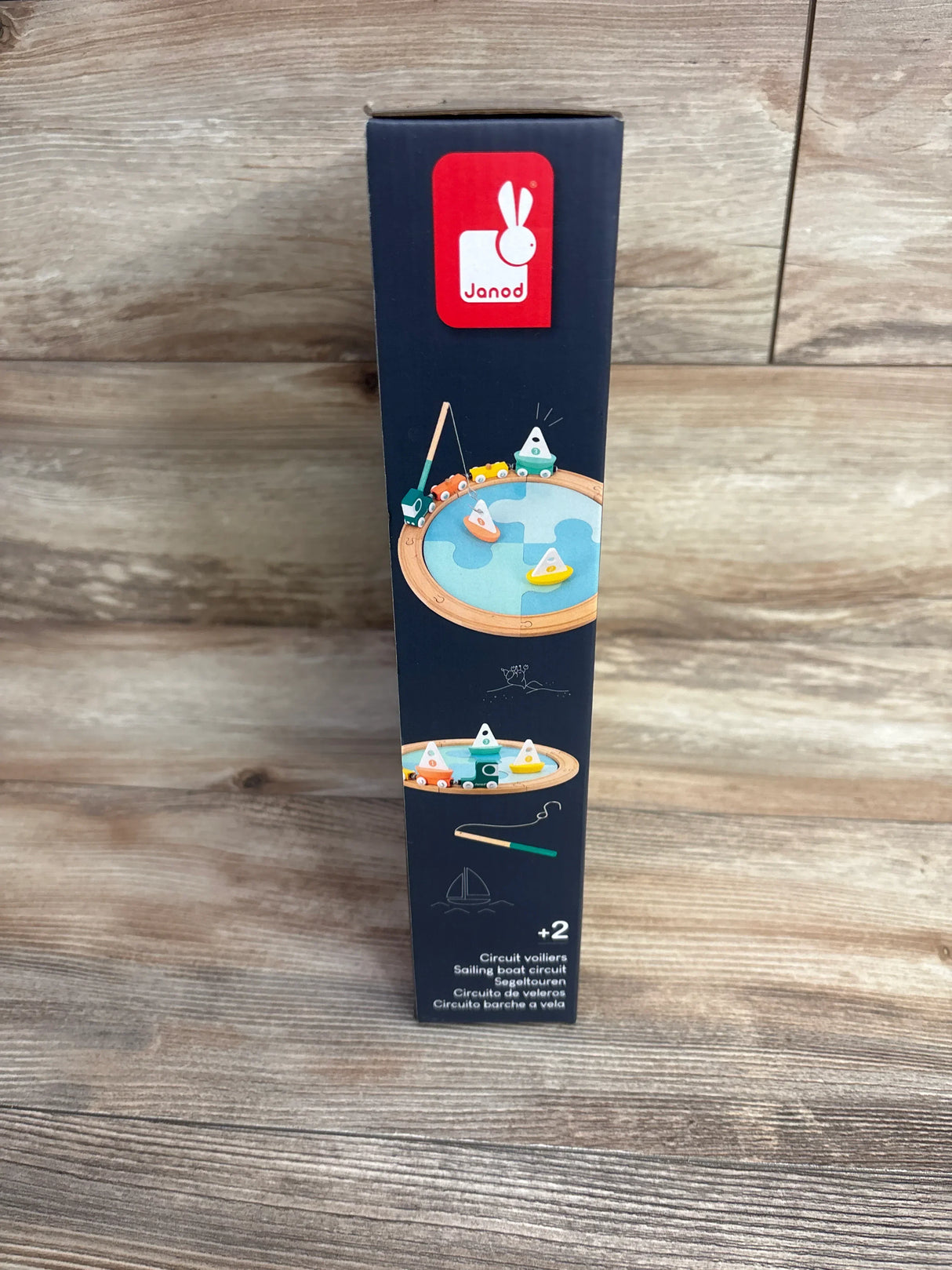 Front view of NEW Janod Sailing Boat Circuit Puzzle Toy box showcasing navy packaging with sailing boat circuit graphic and red logo on wood plank floor