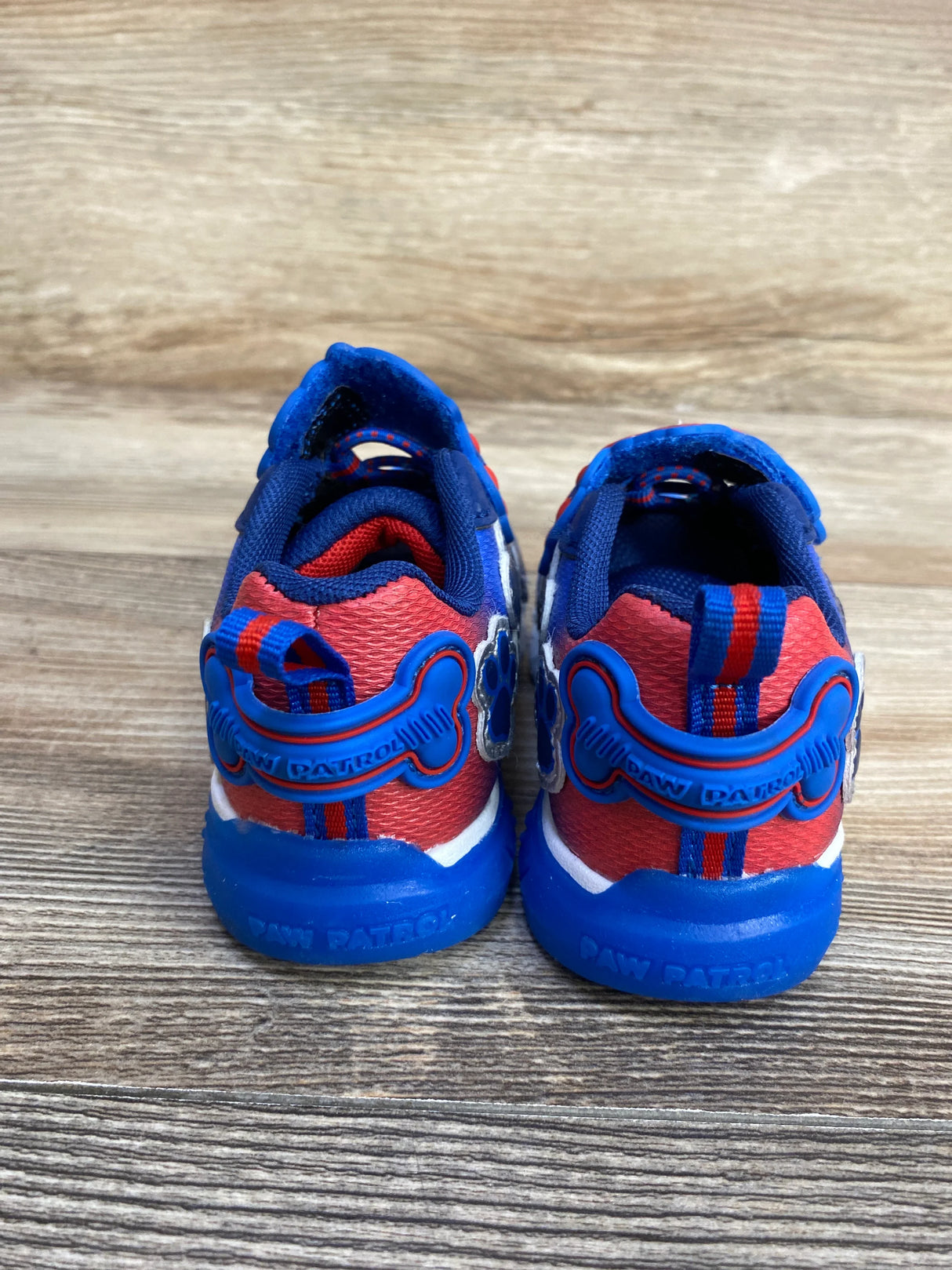 Rear view of children's Paw Patrol sneakers in red, blue, and white on wood floor