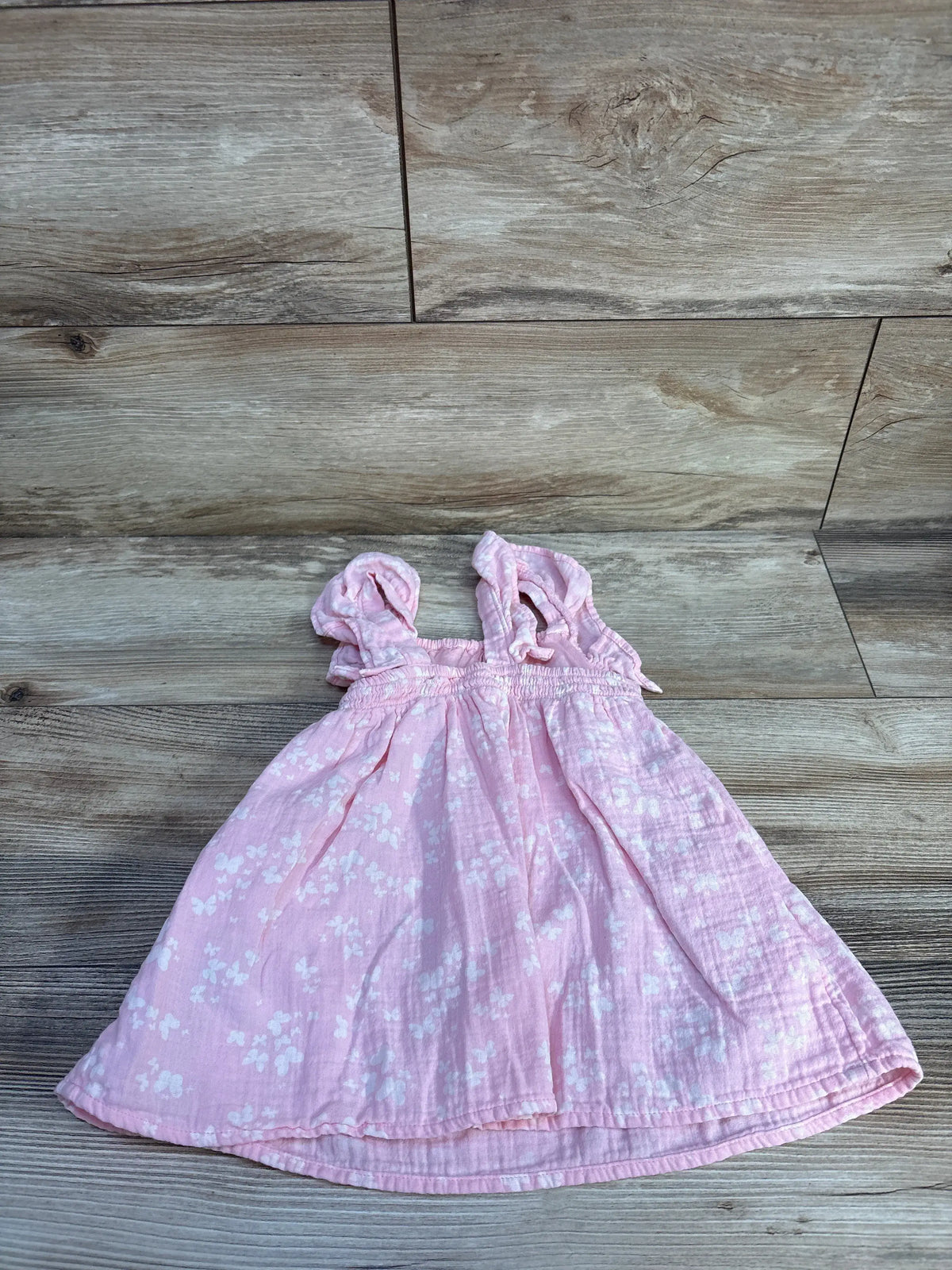 Flat lay view of Cat & Jack smocked gauze dress with pink floral print, smocked upper, and ruffled straps on wood look flooring
