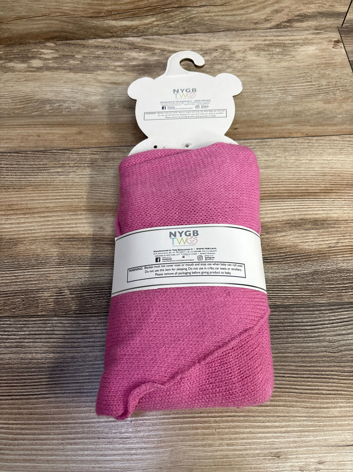Pink baby blanket with NYGB TWOS branding on wooden surface, children's resale store item