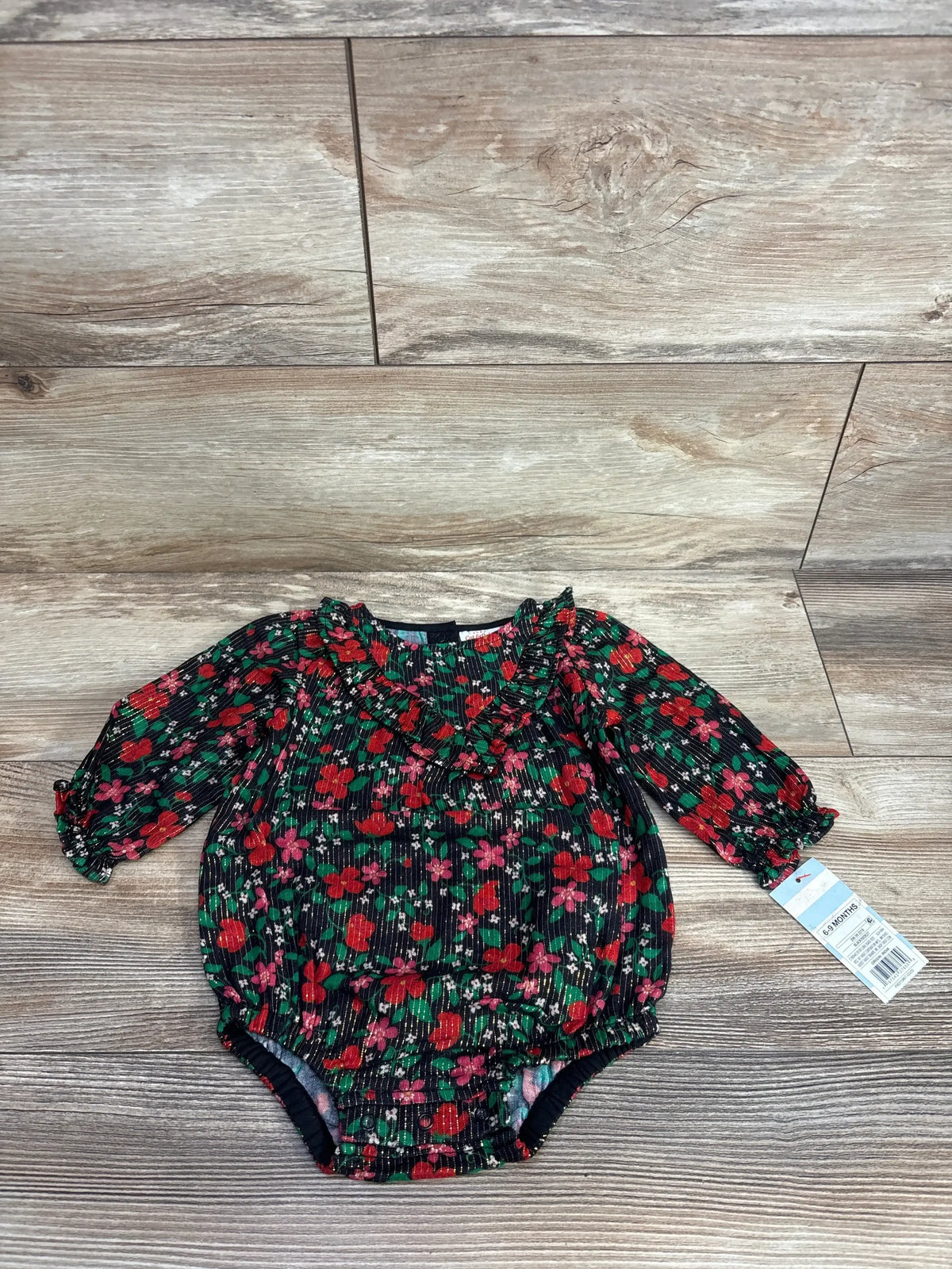 Long sleeve baby romper with red floral print and ruffled neckline on wood background