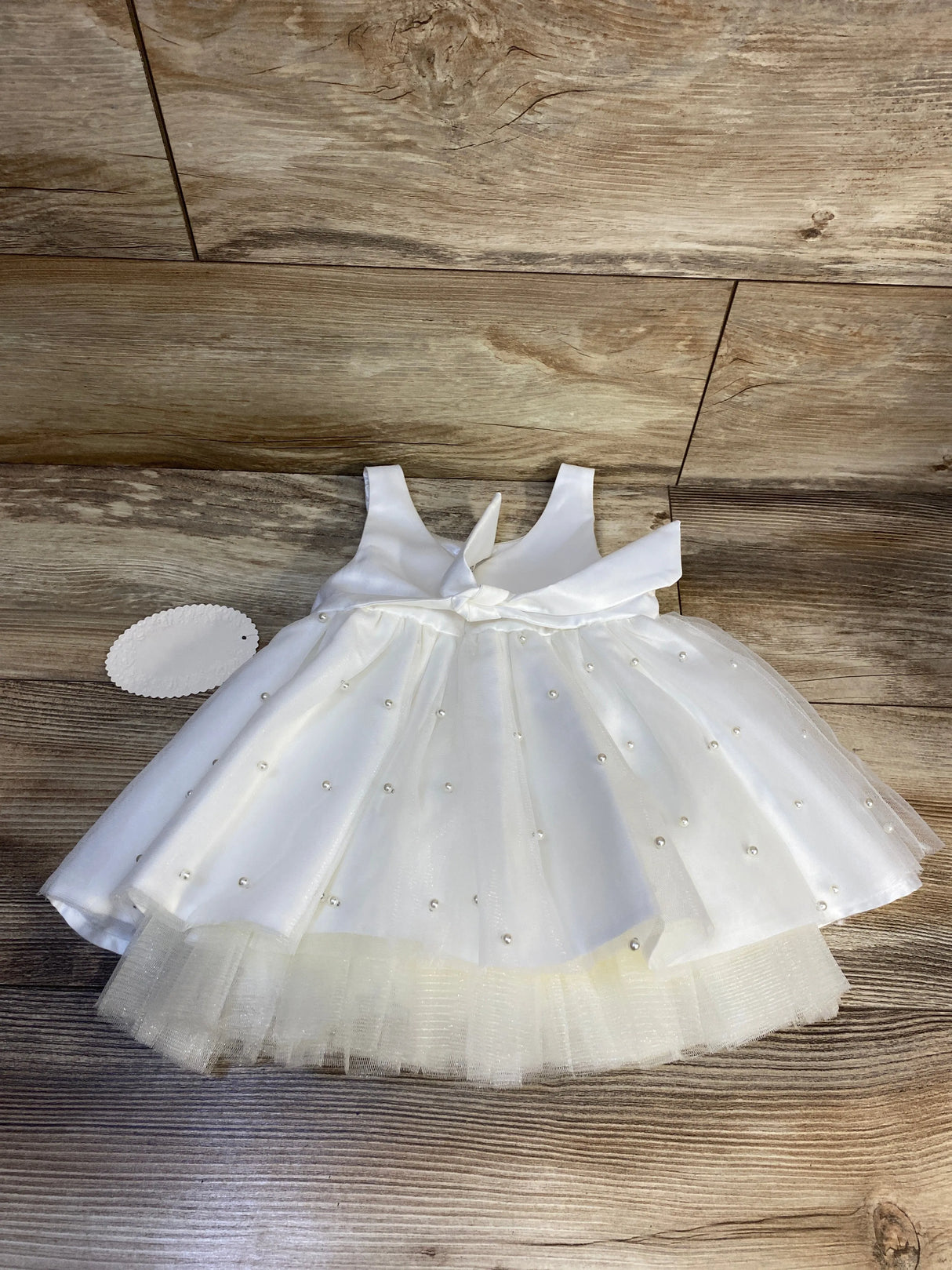 White baby girl dress with pearl details and tulle skirt on wooden floor