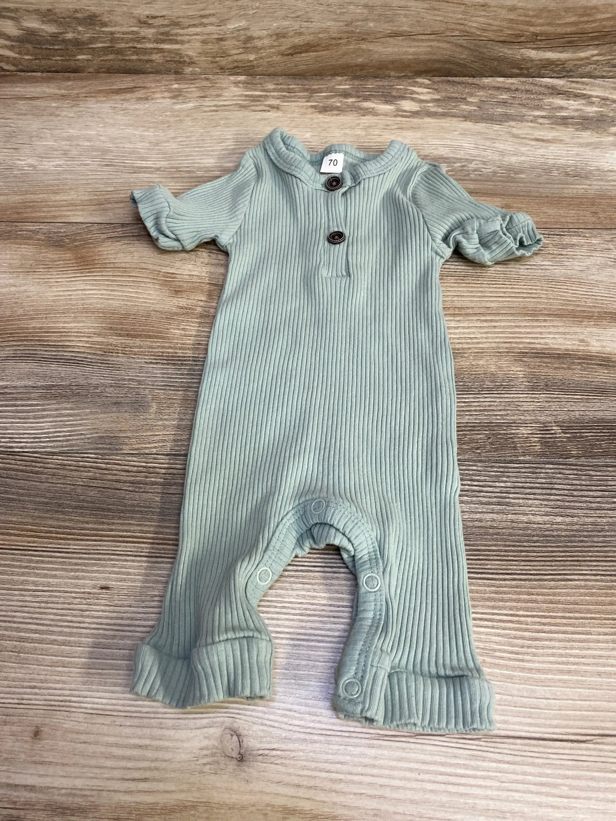 Front flat-lay of green ribbed Henley baby romper with two-button collar, snap crotch, and ruffled cuffs on wood background