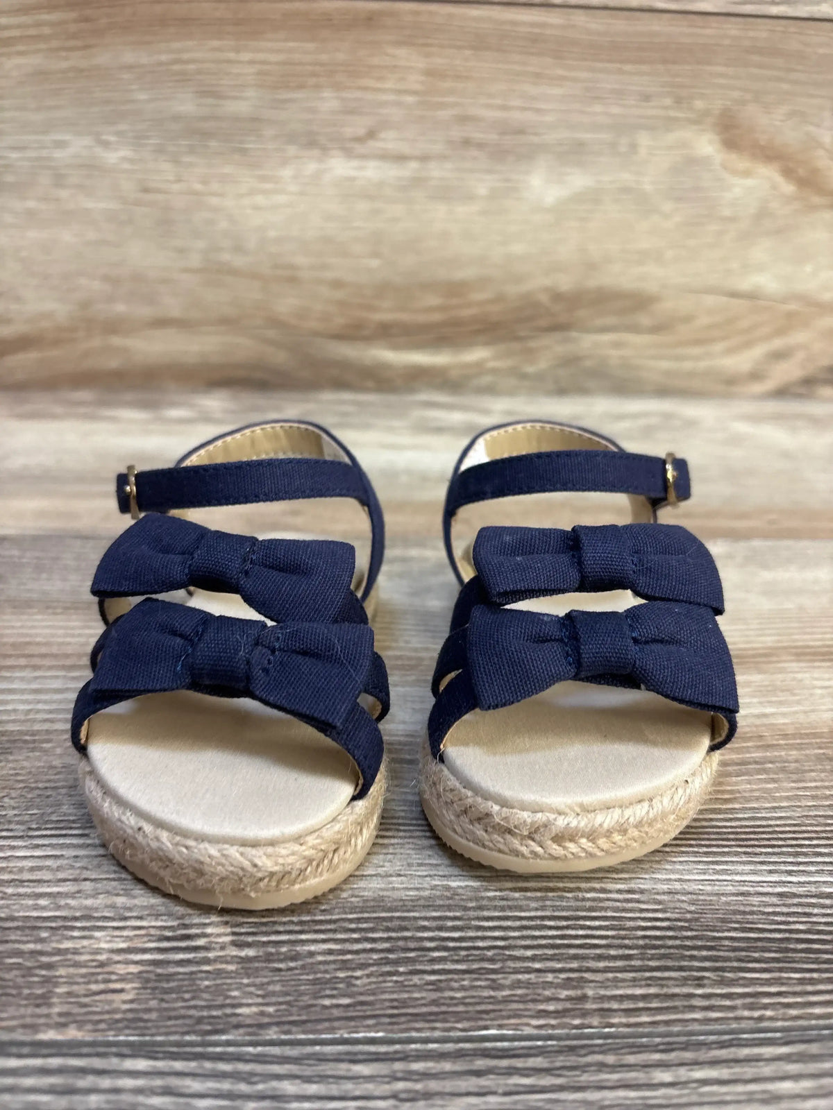 Navy blue toddler sandals with bows and ankle straps on a wood background