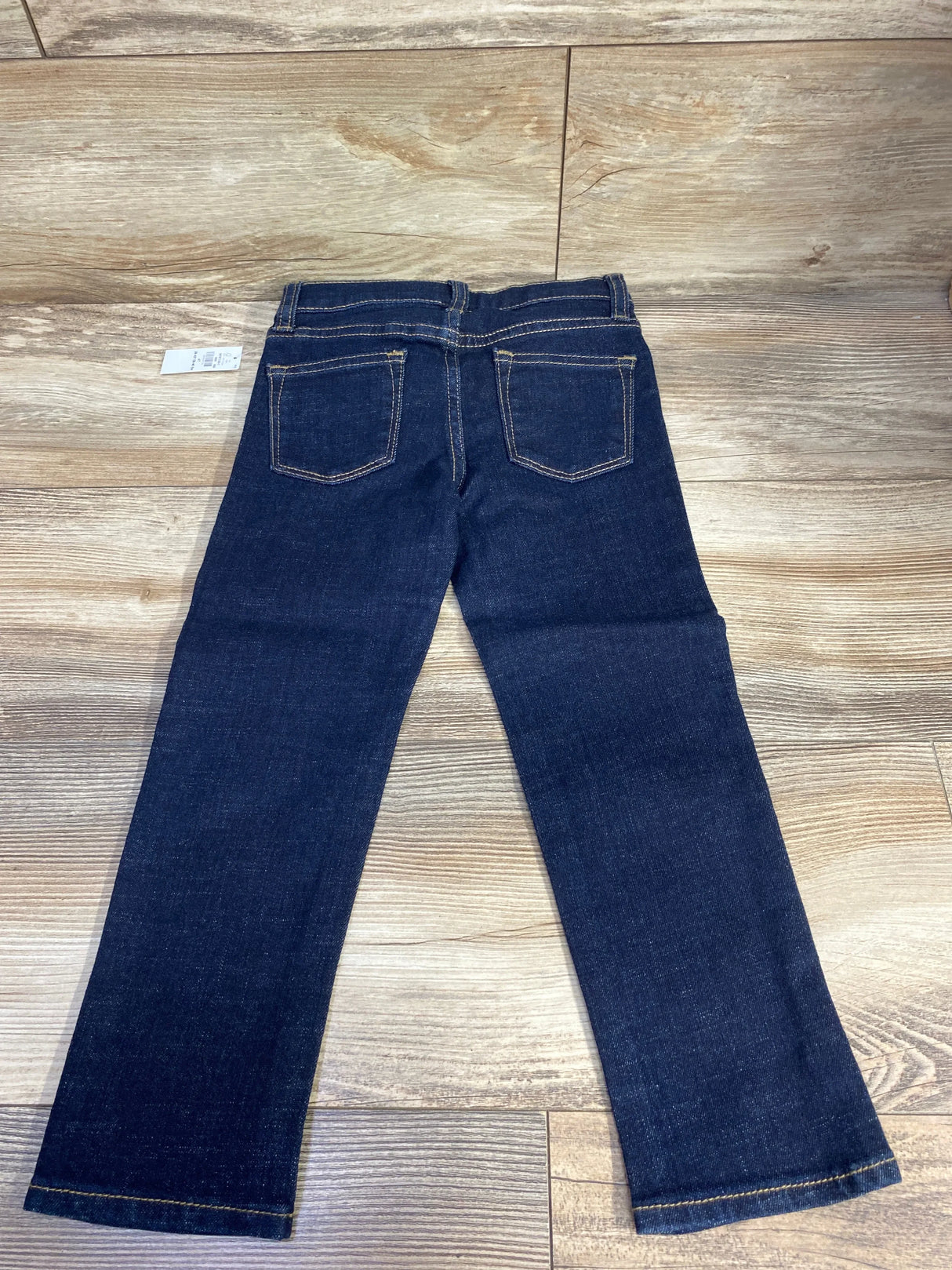Dark blue children's jeans with back pockets on wood floor, gently used kids clothing.