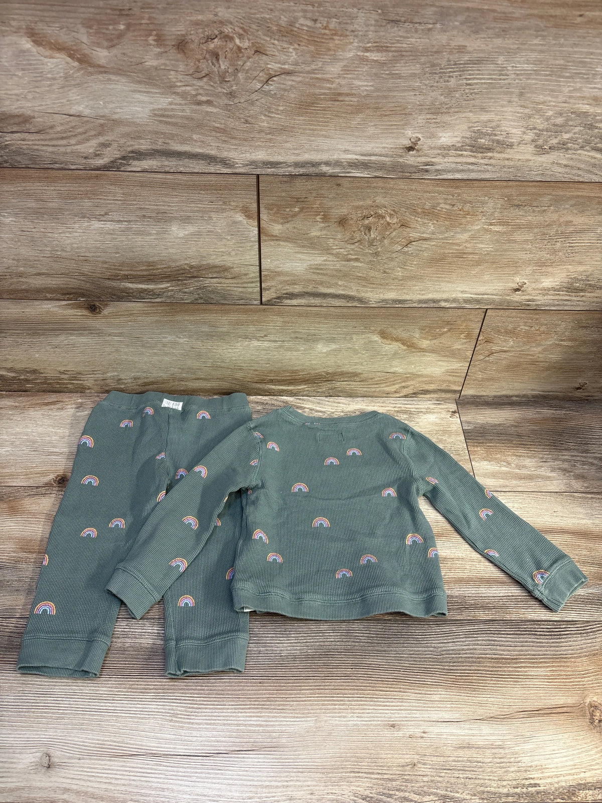 Flat lay of green waffle knit shirt and pants set showcasing rainbow print on a wood-look background