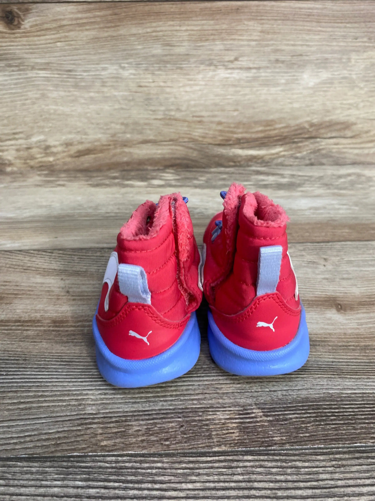 Pair of red toddler Puma shoes with blue soles on wooden floor background