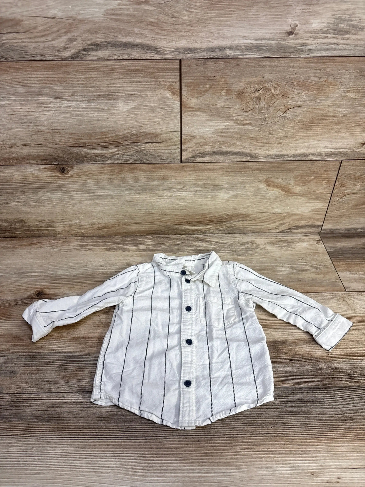 White long-sleeve toddler shirt with black vertical stripes and dark buttons on wood floor