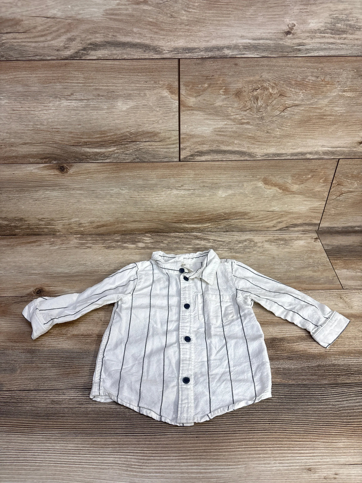 White long-sleeve toddler shirt with black vertical stripes and dark buttons on wood floor