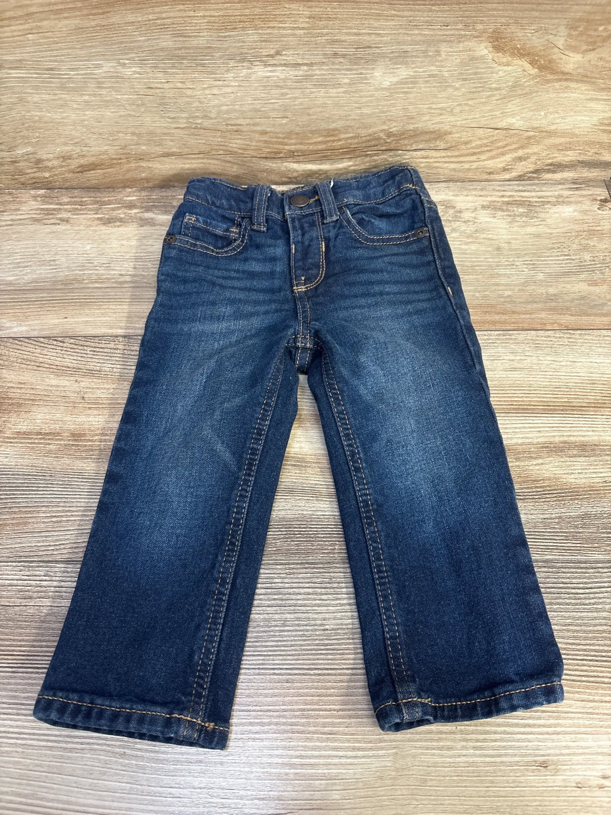 Front flat lay of Old Navy toddler straight-leg blue jeans showing front pockets, faded wash, and straight legs on wood background