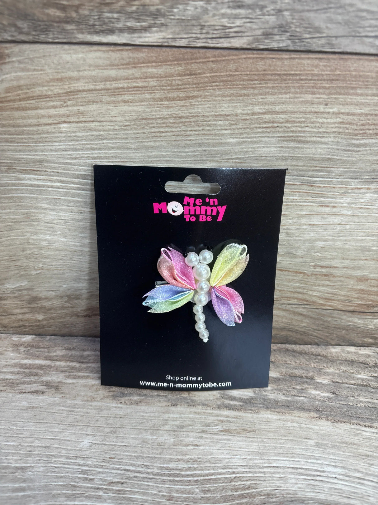 Front view of dragonfly hair bow showcasing pearl bead body and pastel iridescent ribbon wings on black branded card