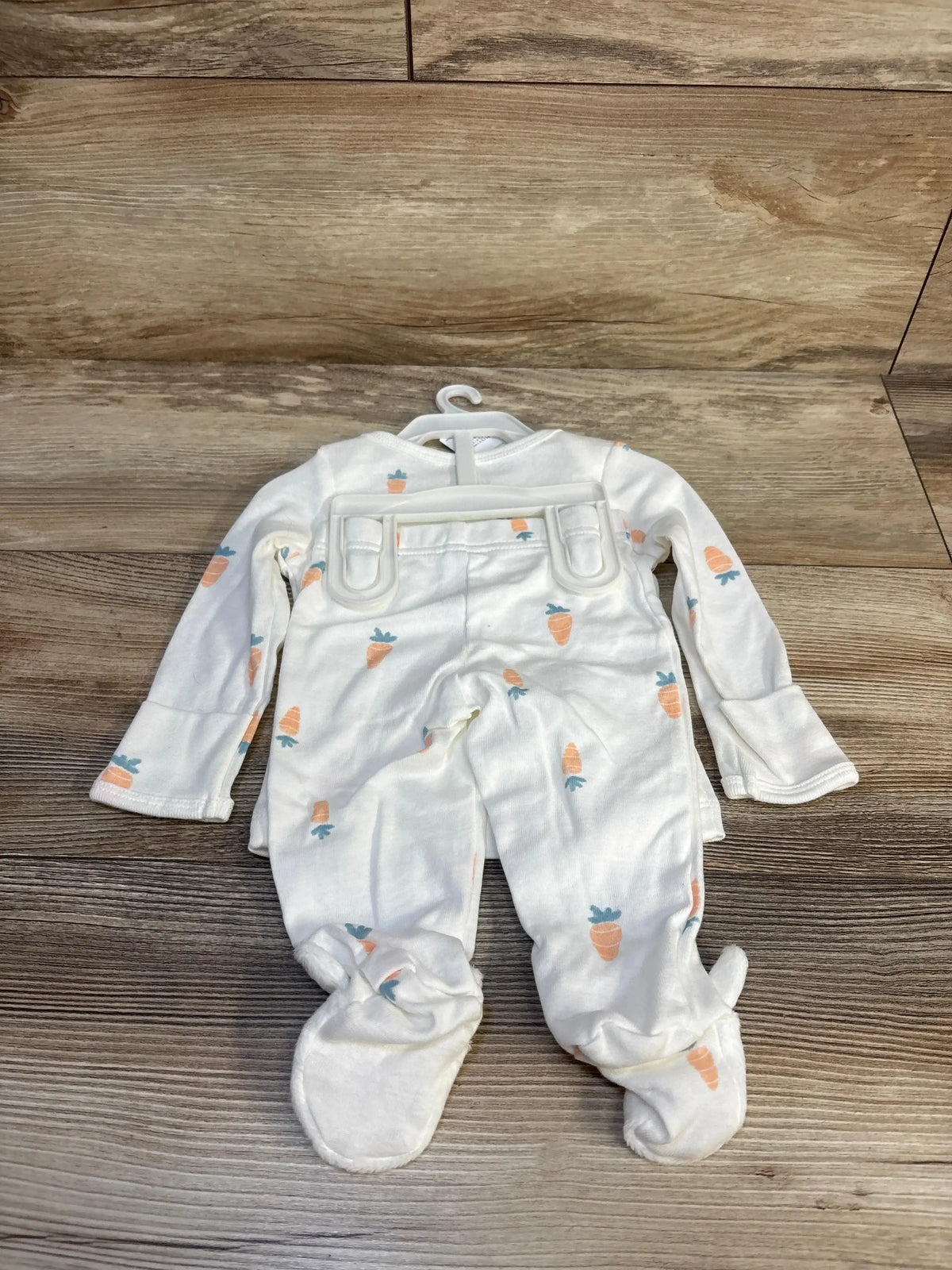 White baby onesie with carrot print, long sleeves, footed, on hanger over wood floor