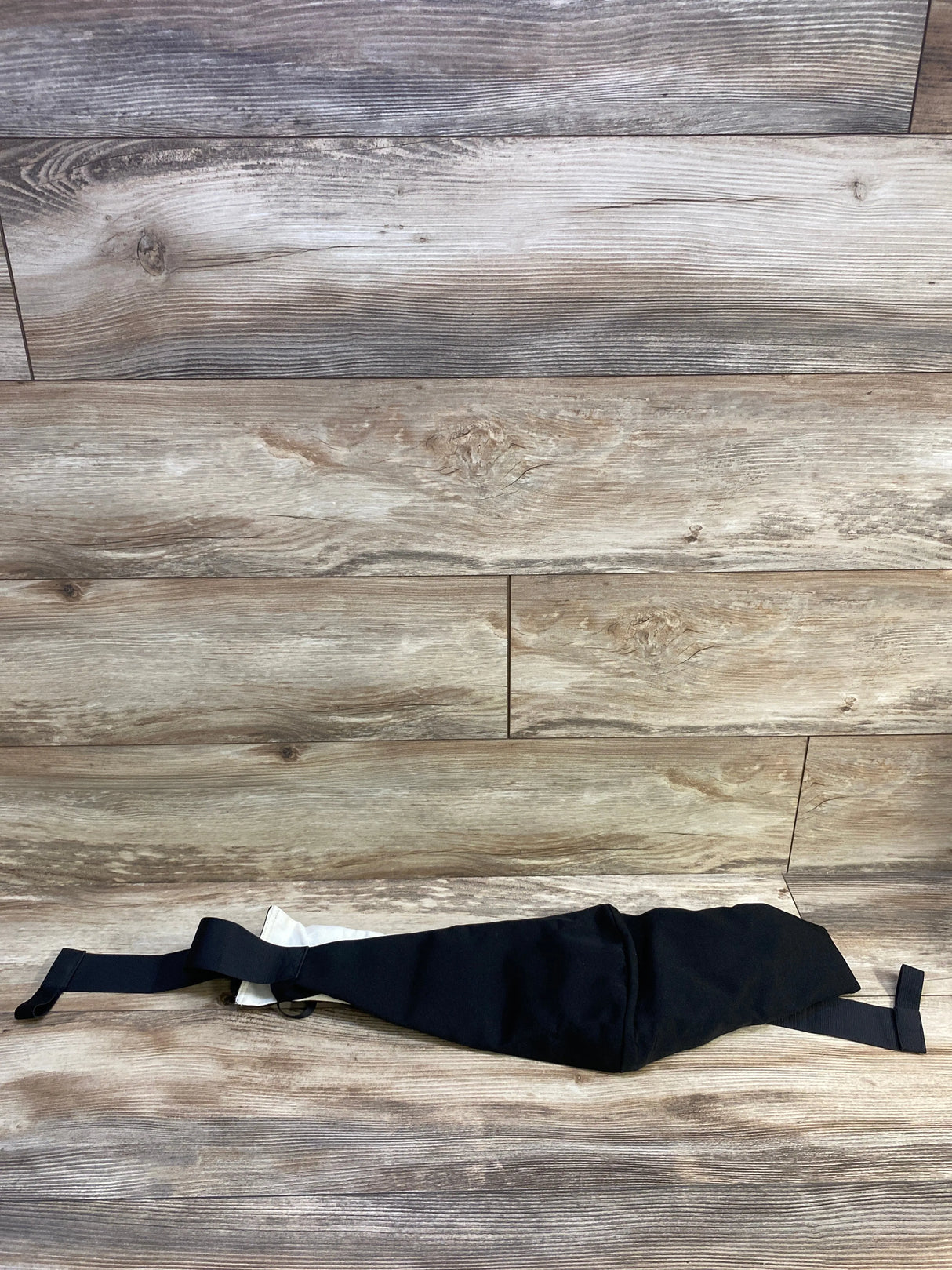 Flat lay of Bambora sling carrier in black showcasing adjustable straps and padded body with light wood background