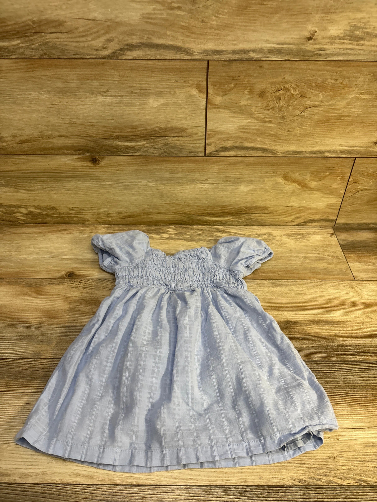Flat lay of Baby Gap blue smocked toddler dress size 4T showing smocked bodice and puff sleeves on wooden floor background