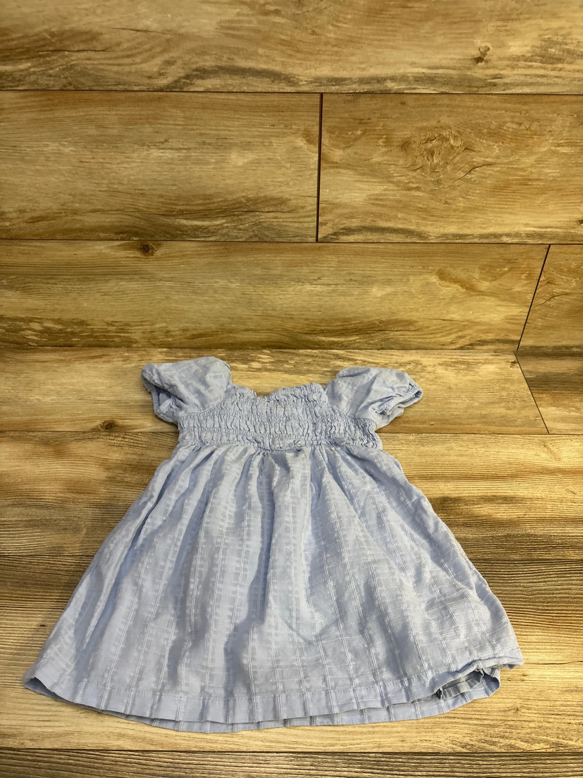 Flat lay of Baby Gap blue smocked toddler dress size 4T showing smocked bodice and puff sleeves on wooden floor background