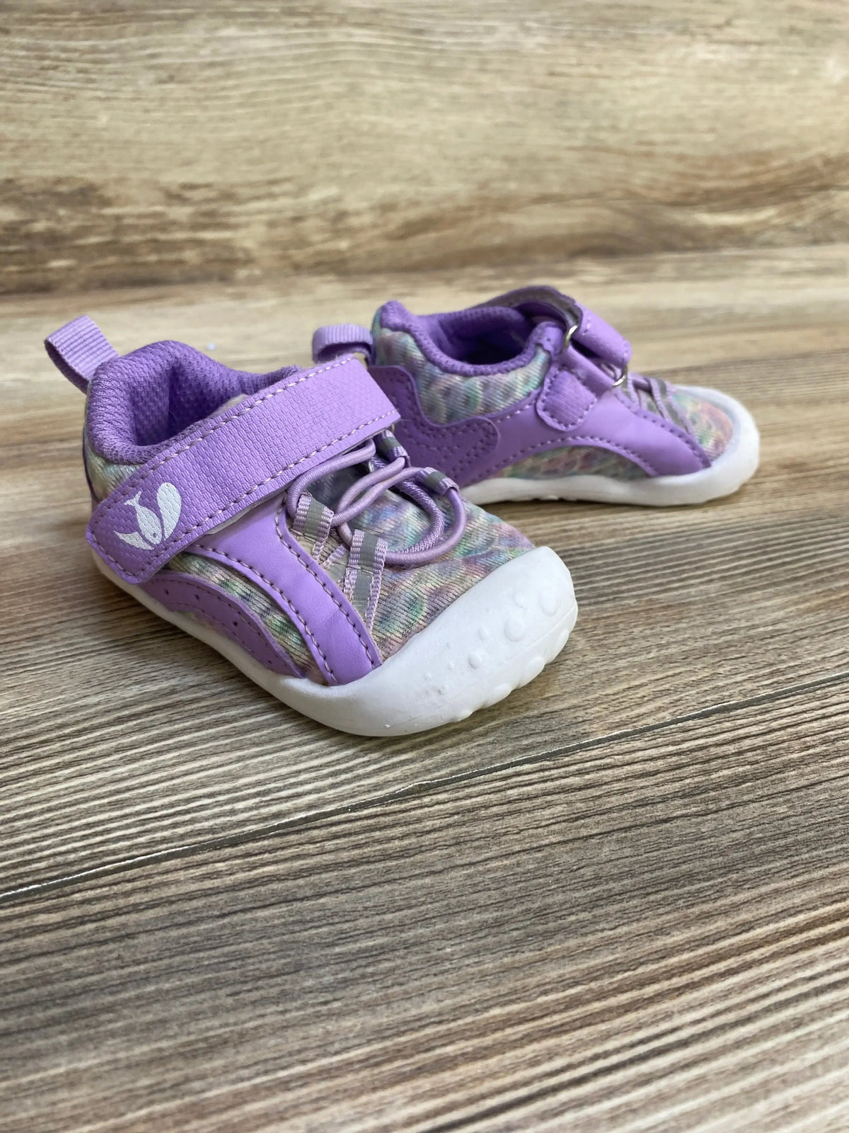 Three-quarter front view of FEETCITY wide barefoot toddler water shoe showing purple velcro strap, multicolor knit upper and white toe bumper on wood floor