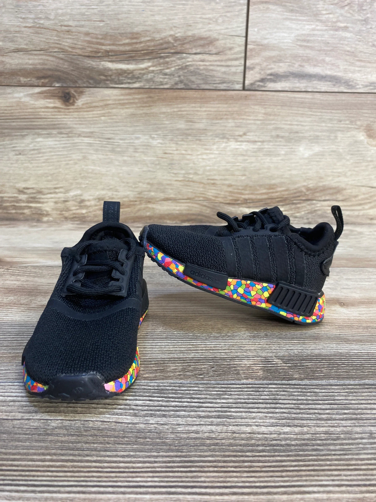 Black kids sneakers with colorful patterned soles on wood background