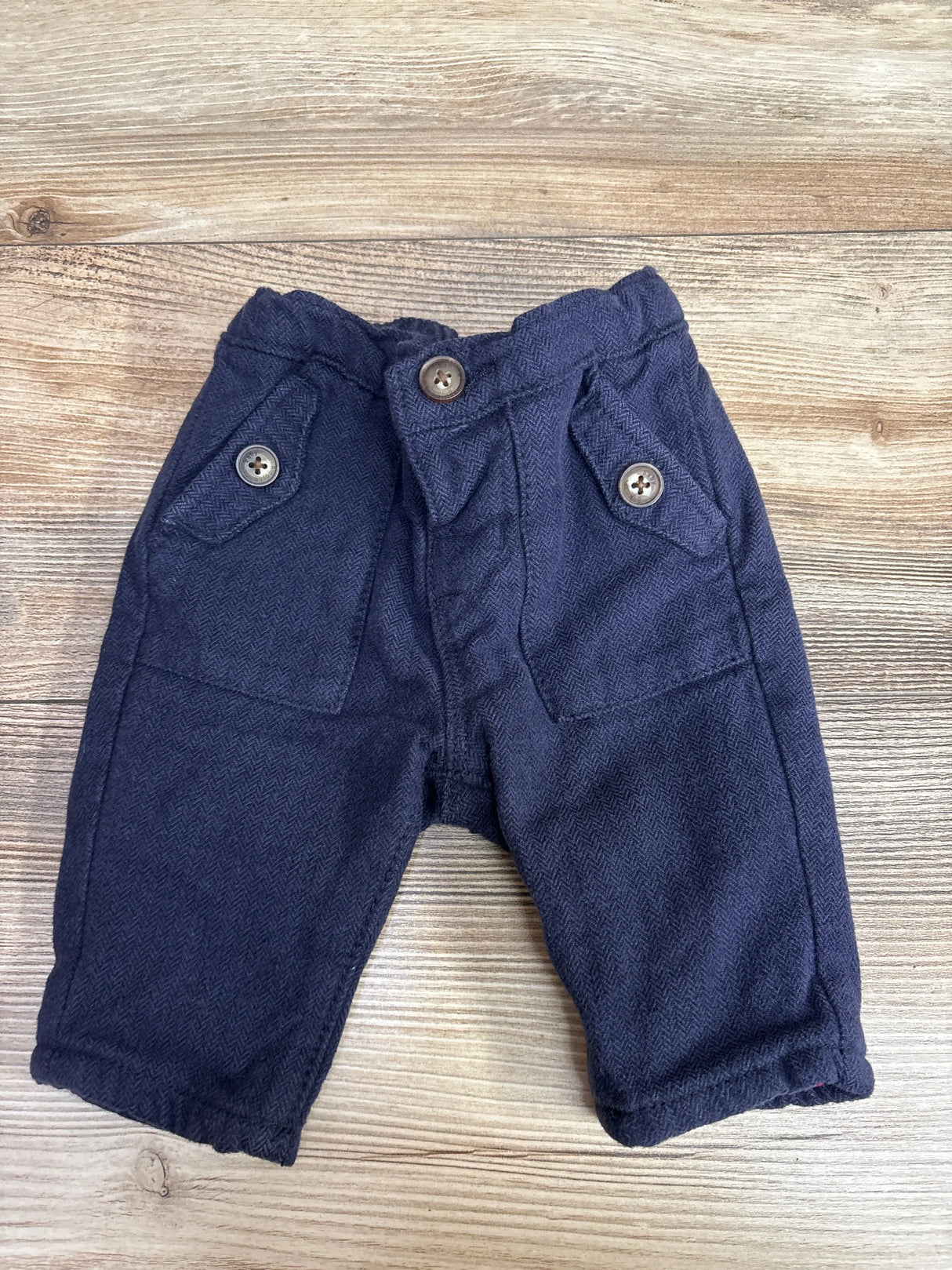 Navy blue baby pants with buttoned pockets on wooden background