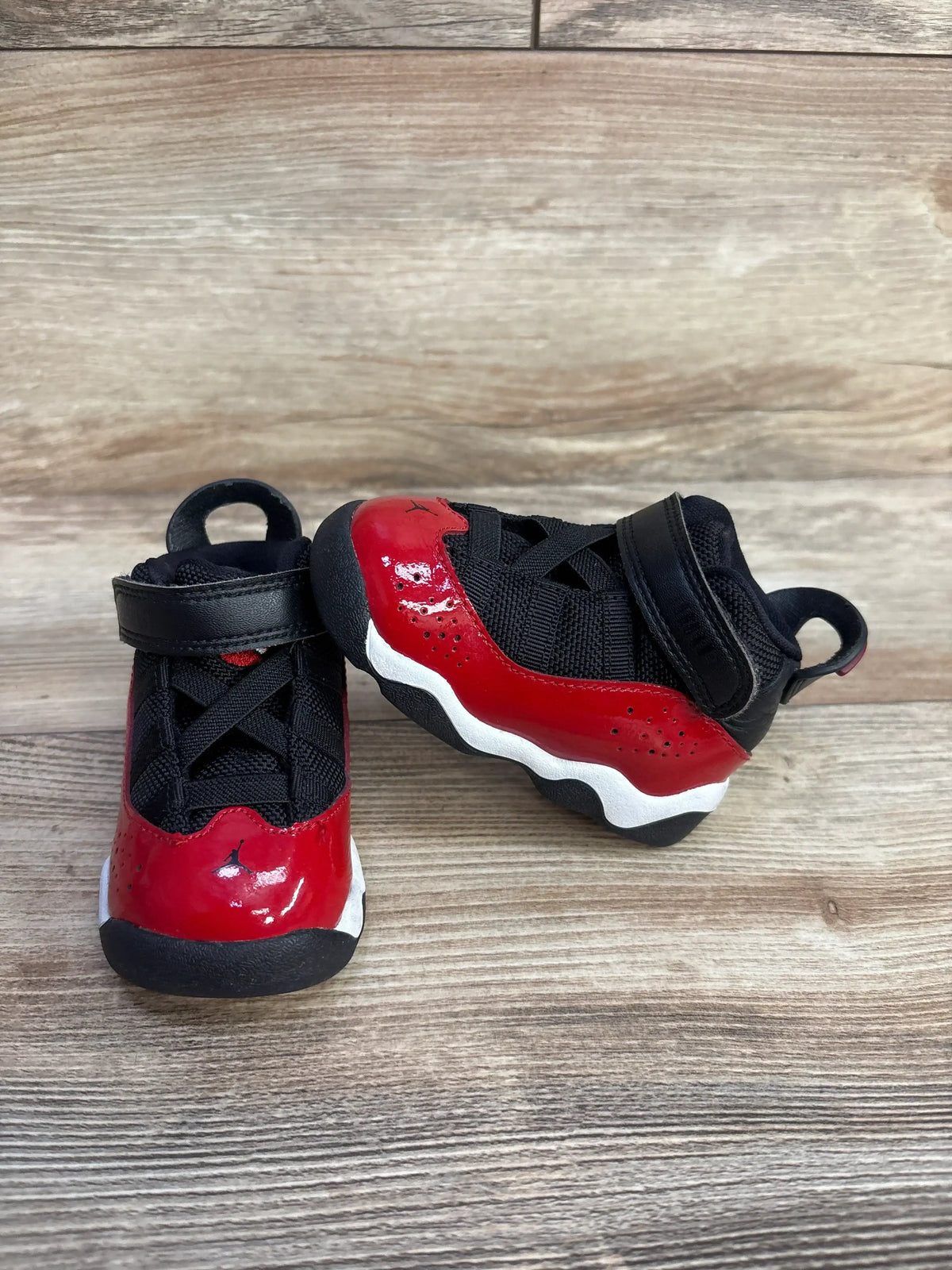 Side-front view of Jordan 6 Rings TD sneakers in Fitness Red/black with patent red overlay and velcro strap on wood