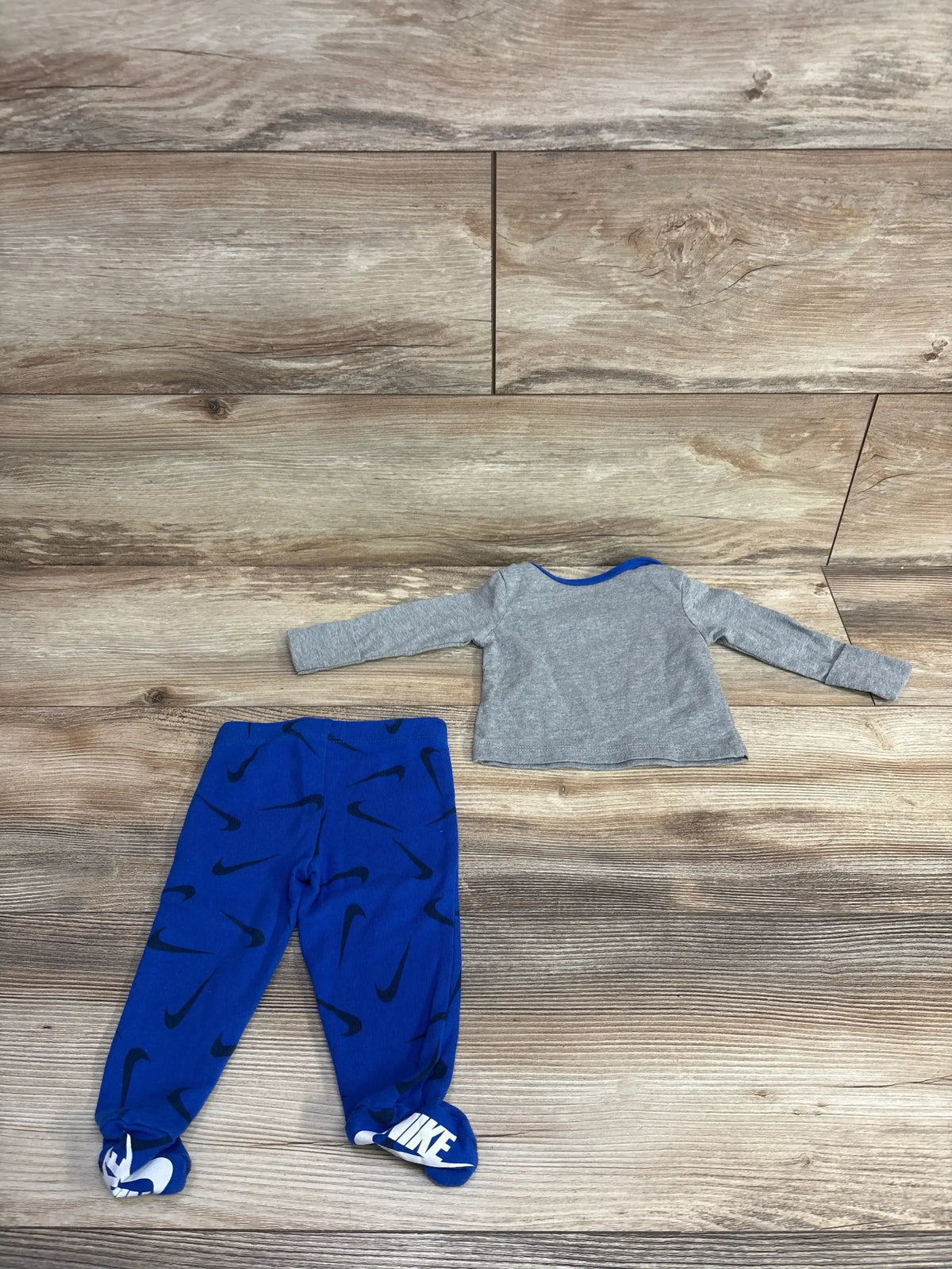 Toddler long sleeve gray shirt and blue Nike footed pants with black swoosh logo on wooden floor
