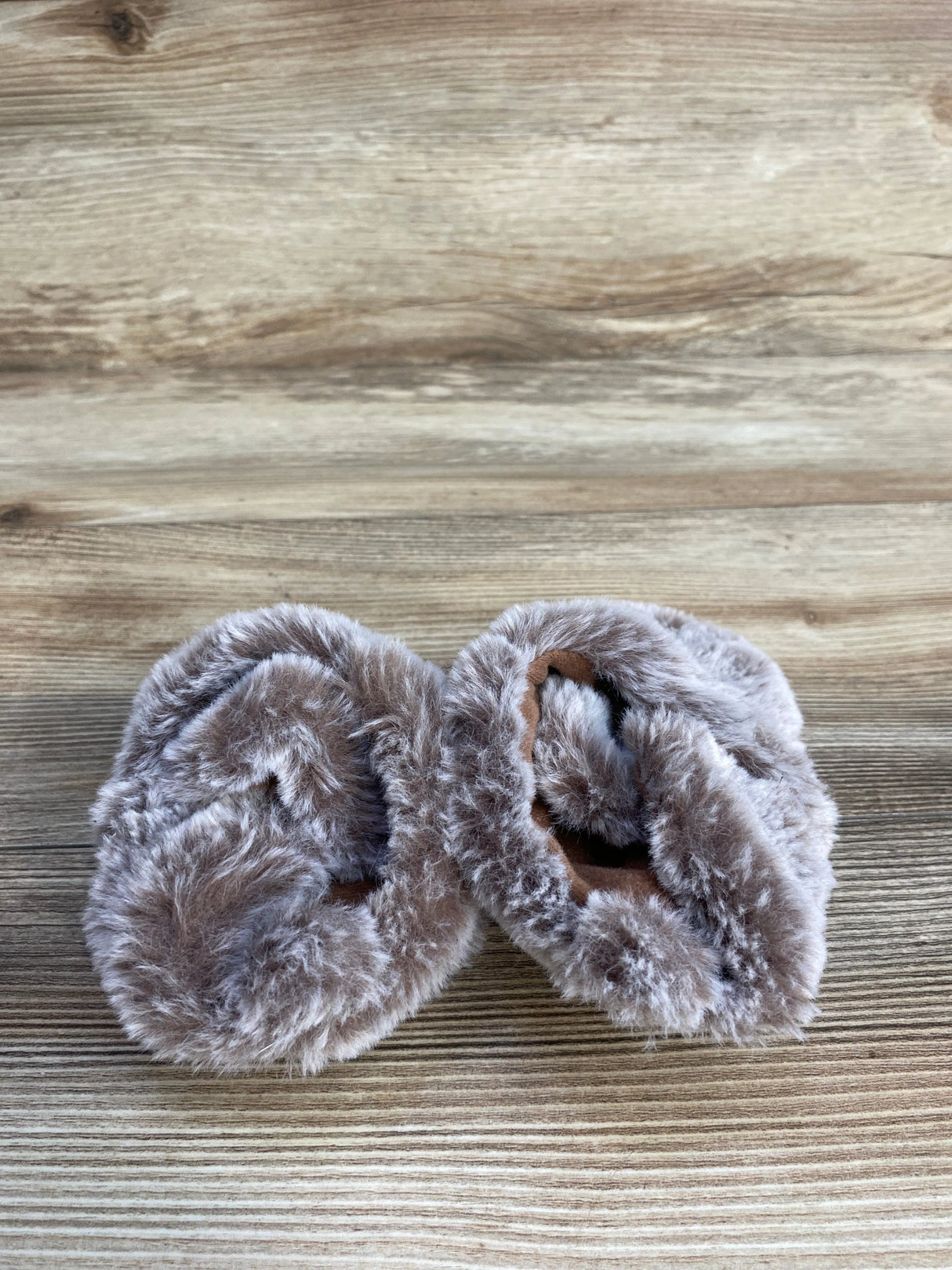 Pair of soft brown faux fur baby booties on wooden surface