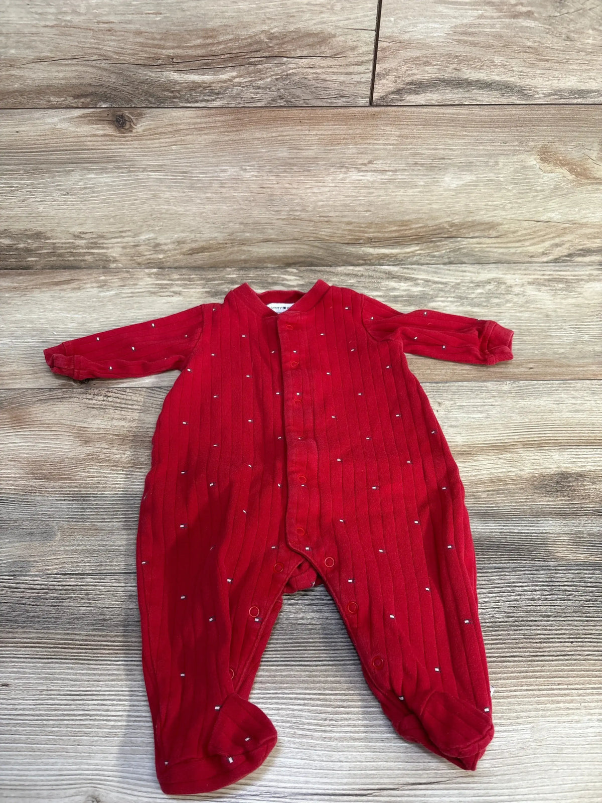 Flat lay of red Tommy Hilfiger baby sleeper 0-3 months showing ribbed knit, snap front and footed legs on wood background