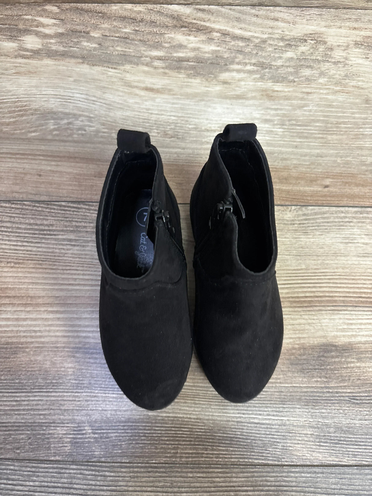 Pair of black suede toddler ankle boots with side zippers on wood floor