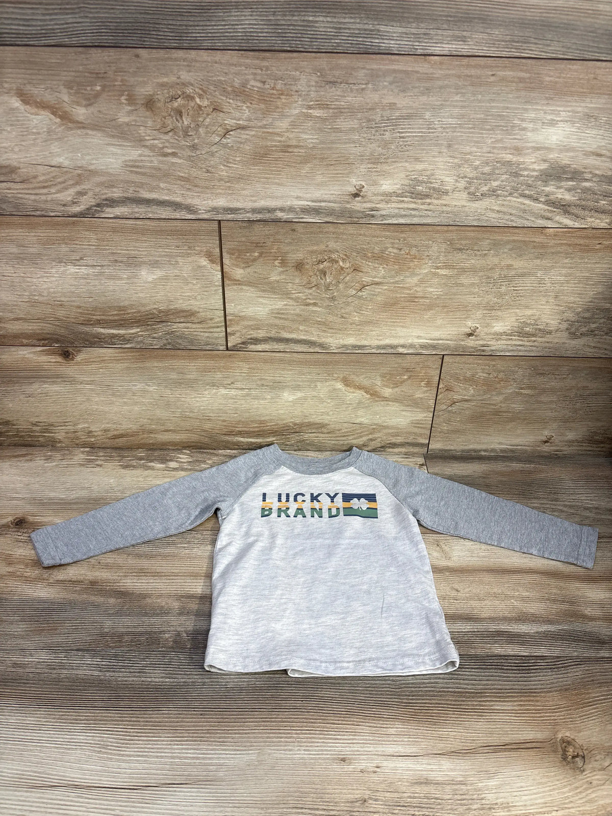 Front view of Lucky Brand grey long sleeve shirt in size 2T showcasing a Lucky Brand graphic with a wood-look background