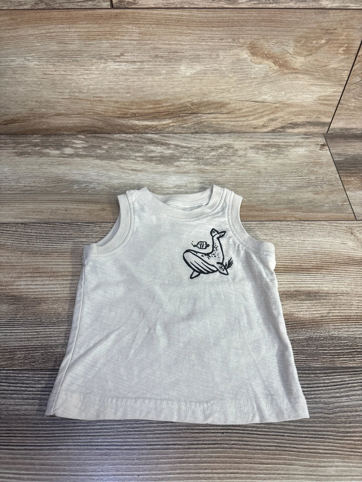 Front view of Carter’s beige tank top in size 3 months showcasing a sleeveless design and black animal graphic on a wood-look background