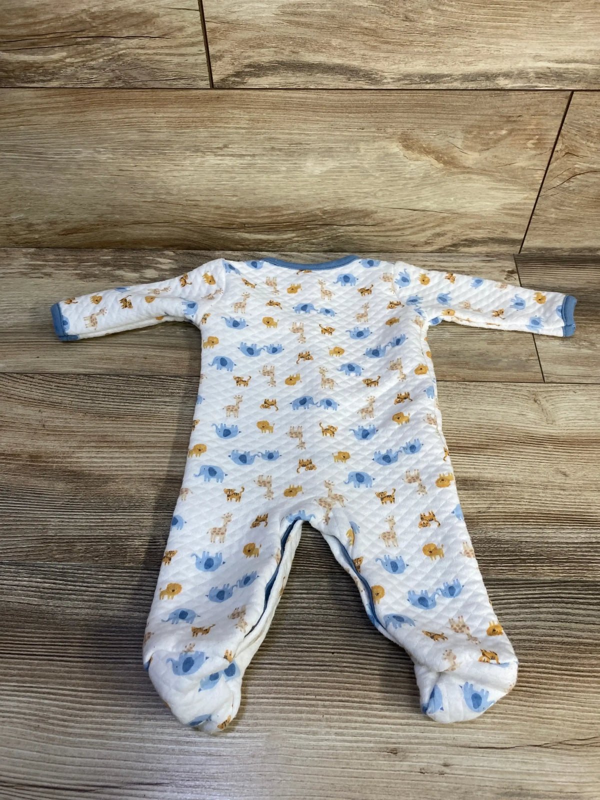 Front view of quilted white baby sleeper size 0 to 3 months showing blue trimmed neckline, footed legs, and animal print on wood floor background
